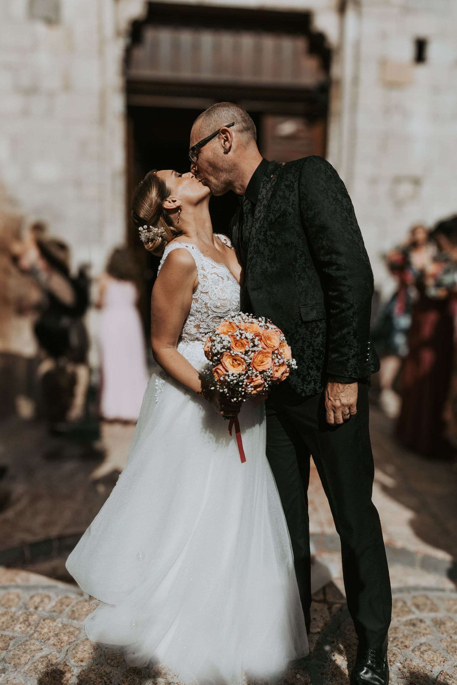 A romantic wedding couple shares tender moments on a cobblestone street in their elegant white dress and black suit.