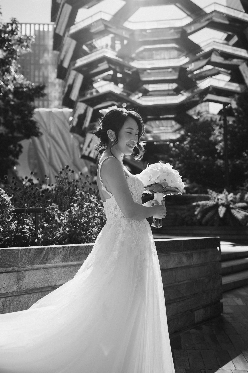A bride holding a bouquet poses outdoors under a modern architectural structure.