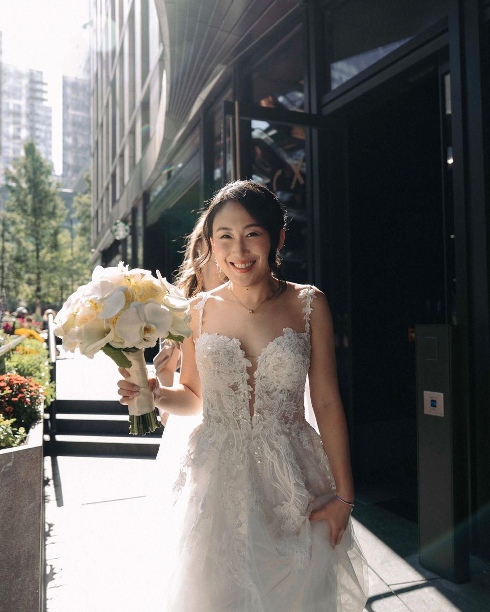 Person in a white wedding dress holding a bouquet outside a modern building.