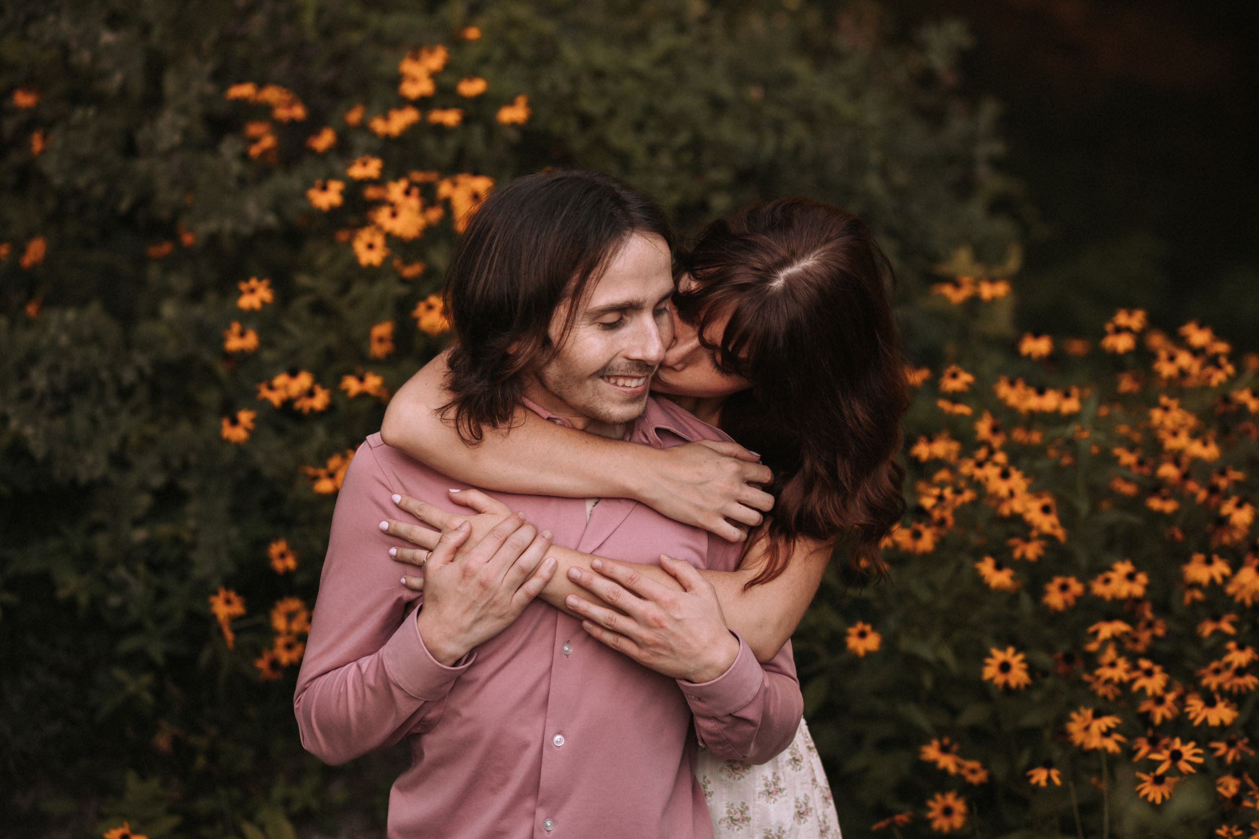 A tender embrace captured in front of orange wildflowers during golden hour.