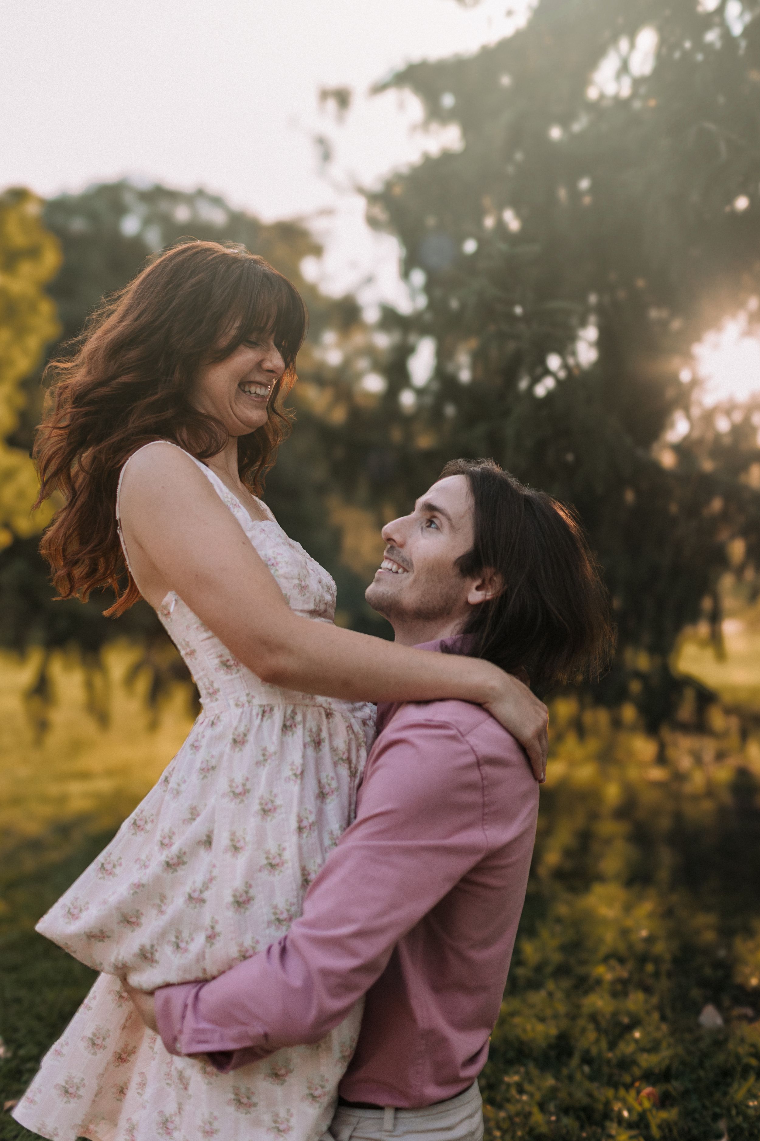 A playful moment captured between a couple in a floral dress and pink sweater at sunset.