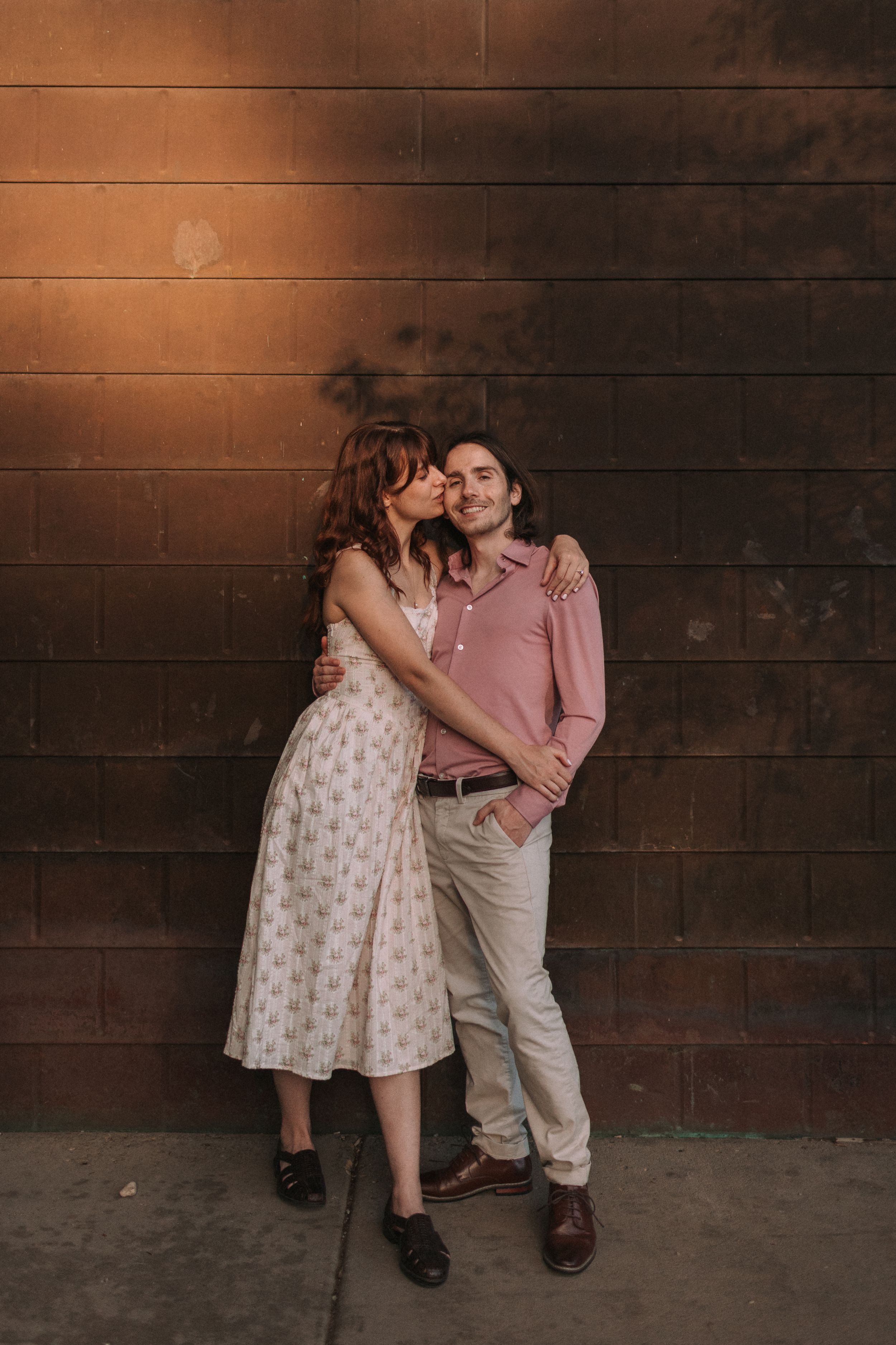 A couple in vintage-inspired outfits shares tender moments against a rustic metal wall in a series of romantic poses.