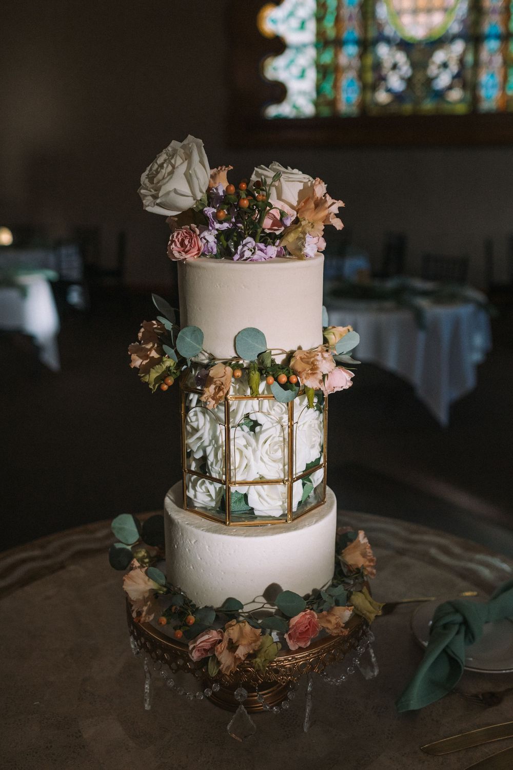Elegant white wedding cake decorated with peach and pink flowers and gold geometric accents.