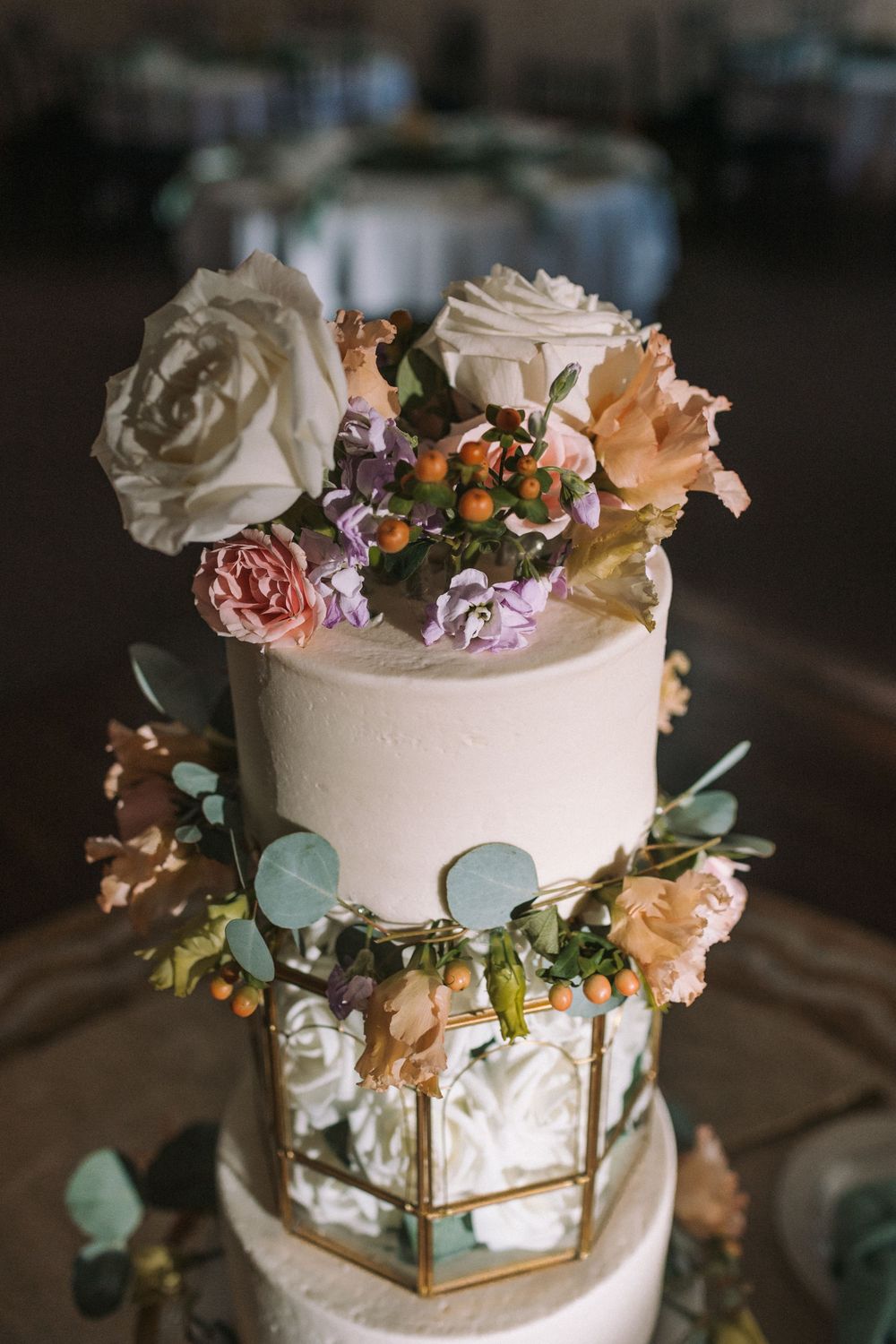 Three-tiered white wedding cake with floral decorations and geometric gold details.