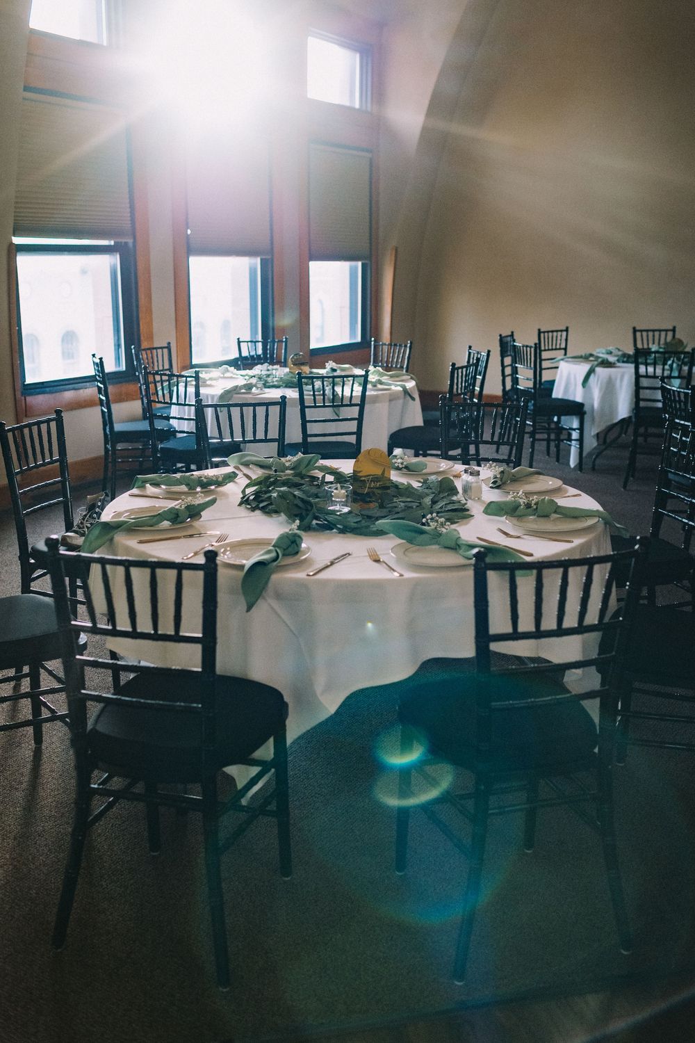 Wedding reception venue with dark chairs and round tables set up in a dimly lit room.