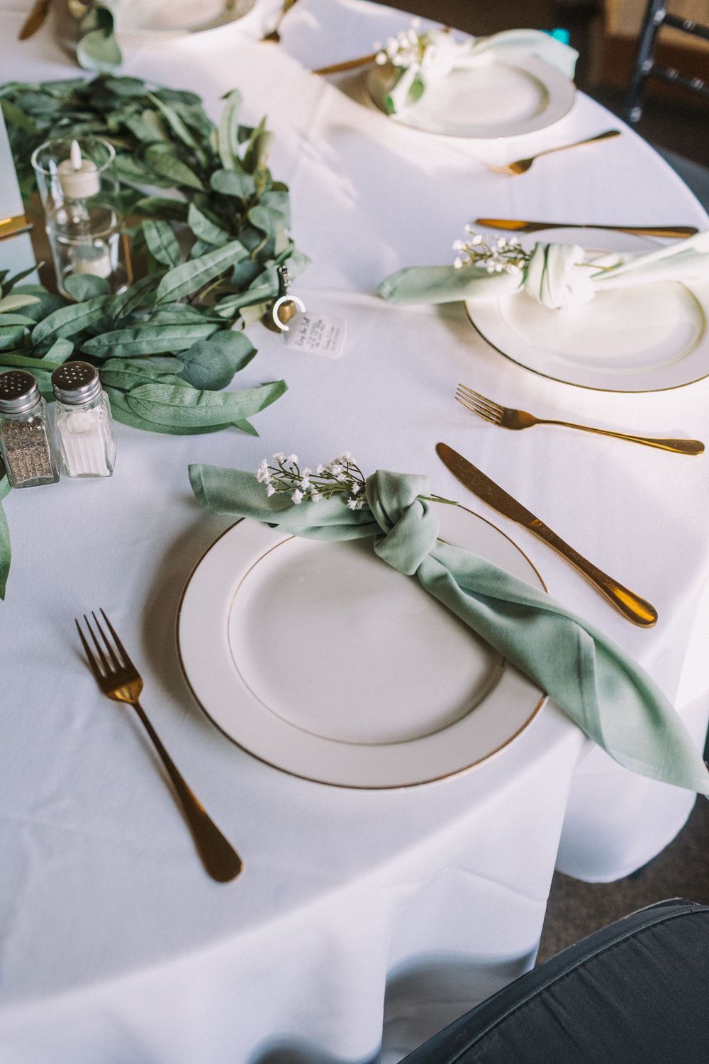 Elegant table setting with white linens, sage green napkins, and gold flatware.