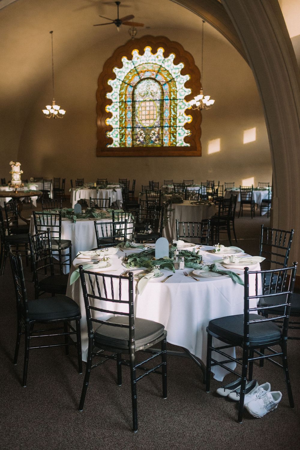 Wedding reception hall with stained glass windows, arched ceiling, and black chiavari chairs.