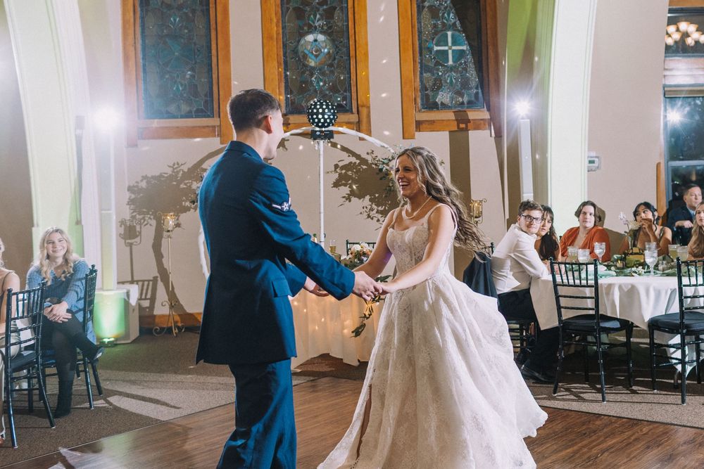 Wedding guests dance and celebrate on a wooden dance floor during an indoor reception.