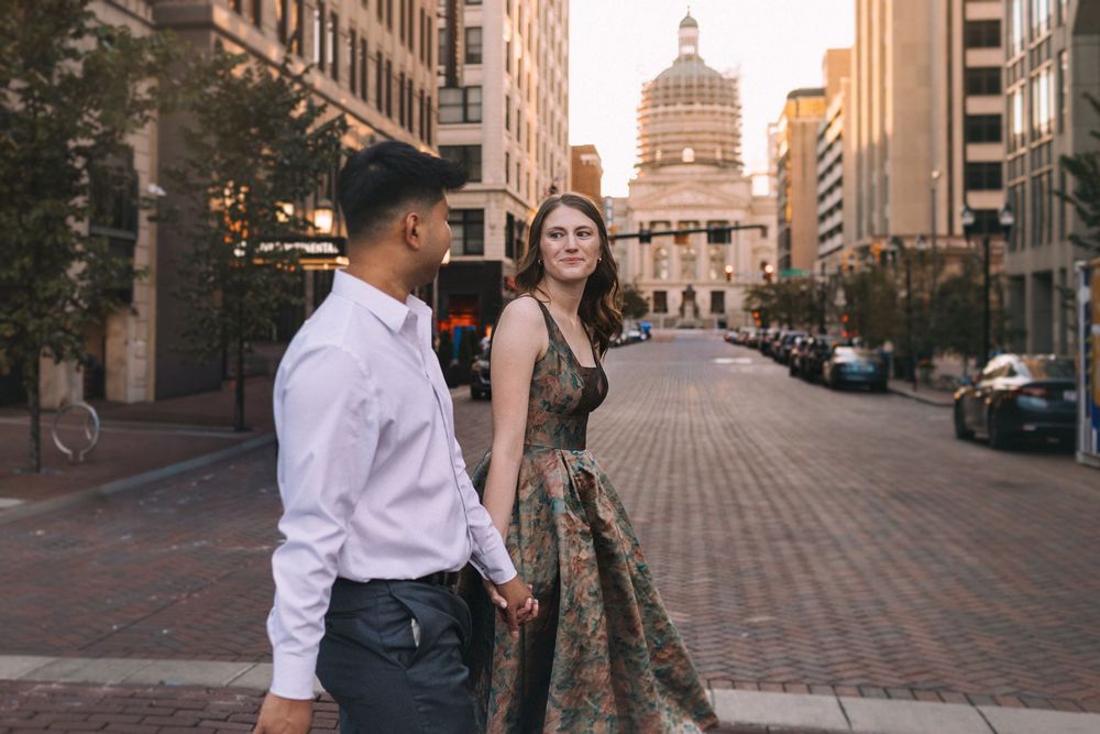 Couple in formal attire posing on city street with historic building in background.