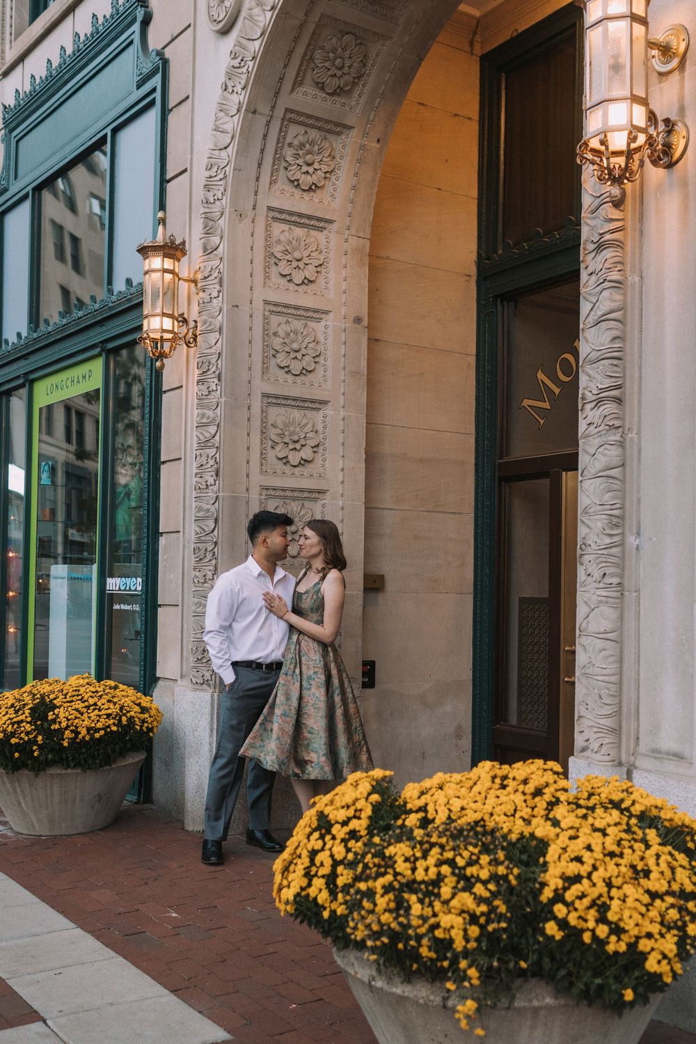 Romantic couple posing by yellow mums and classical architecture with warm evening lighting.