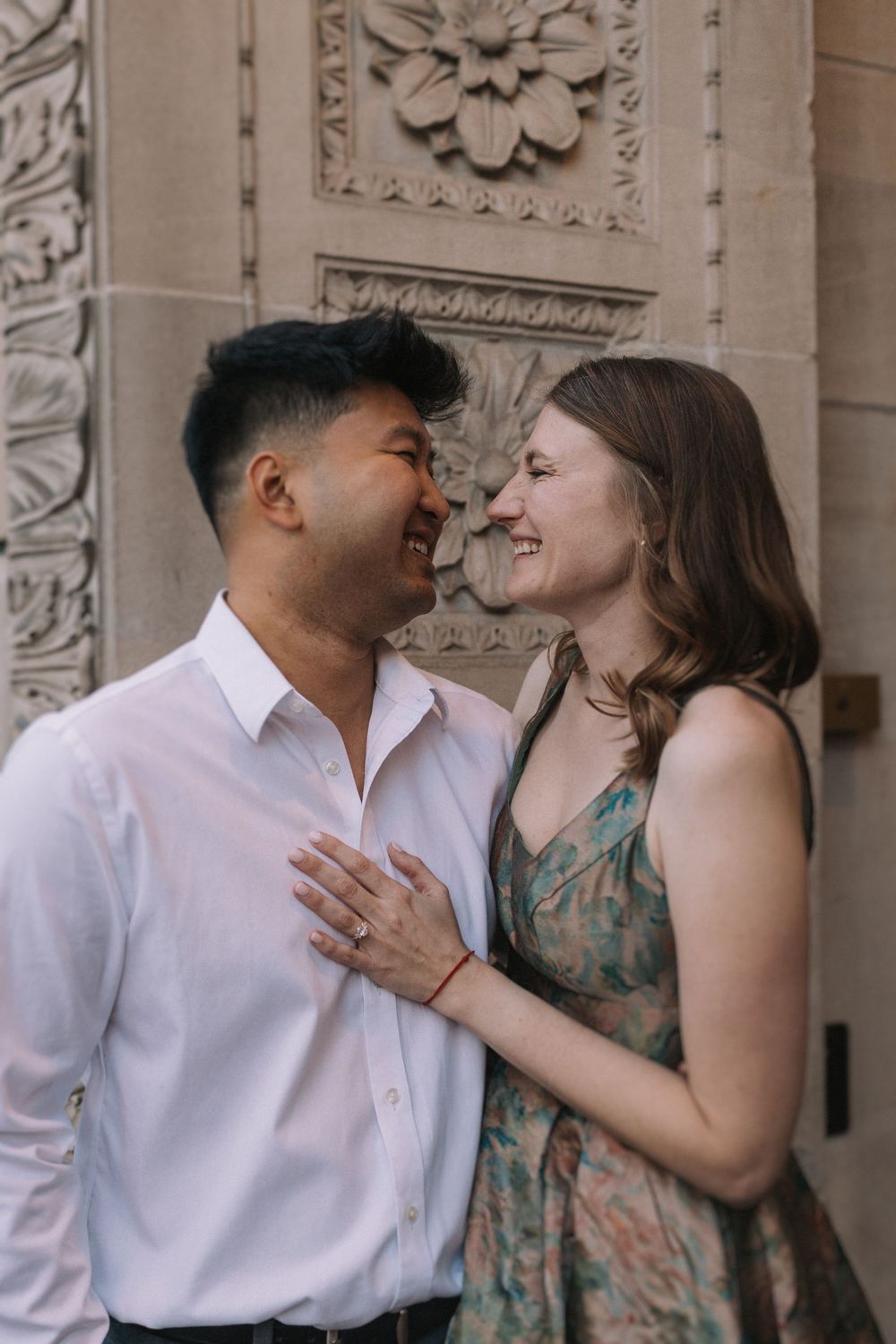Couple sharing joyful laughter against an ornate architectural backdrop with decorative stone details.