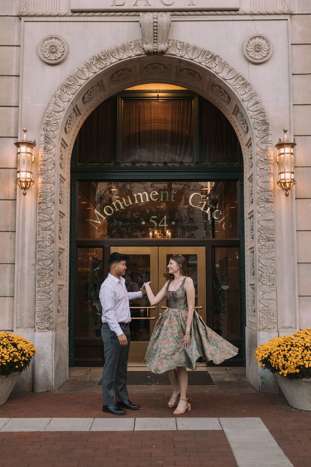 A couple dancing in front of an ornate arched doorway of Monument Circle with yellow flowers decorating the entrance.