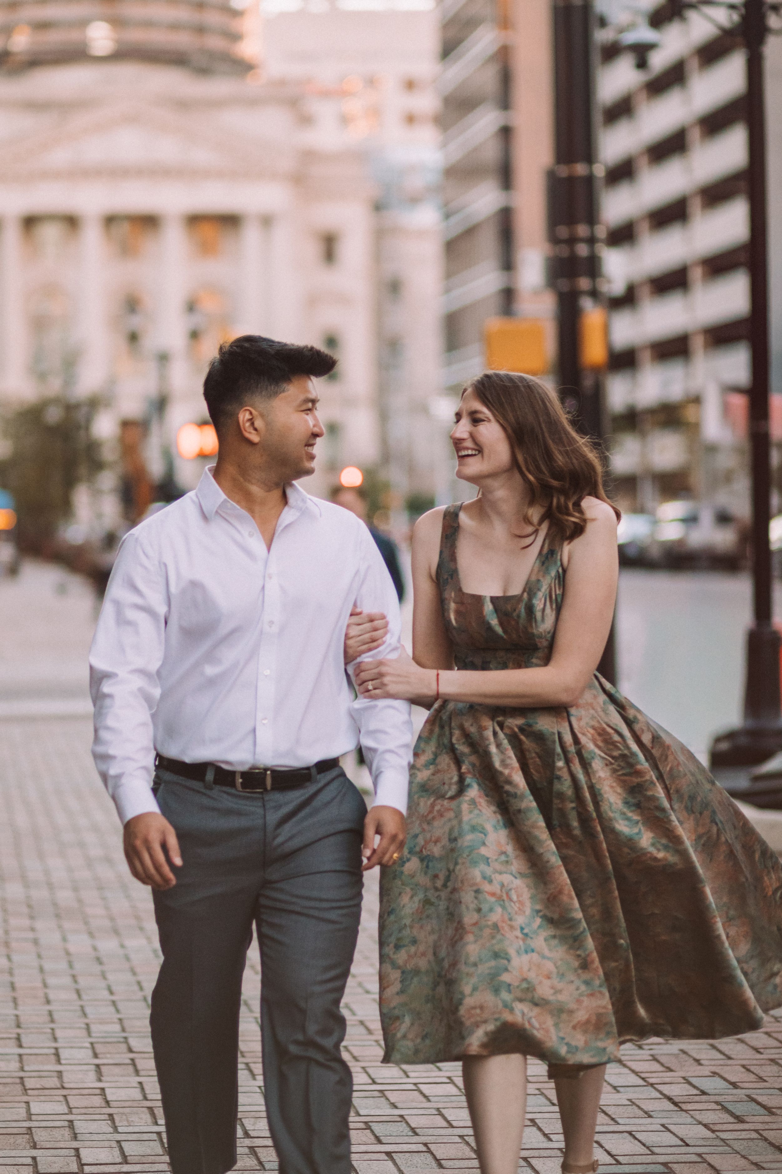 Couple walking and laughing together on cobblestone street during evening photoshoot.