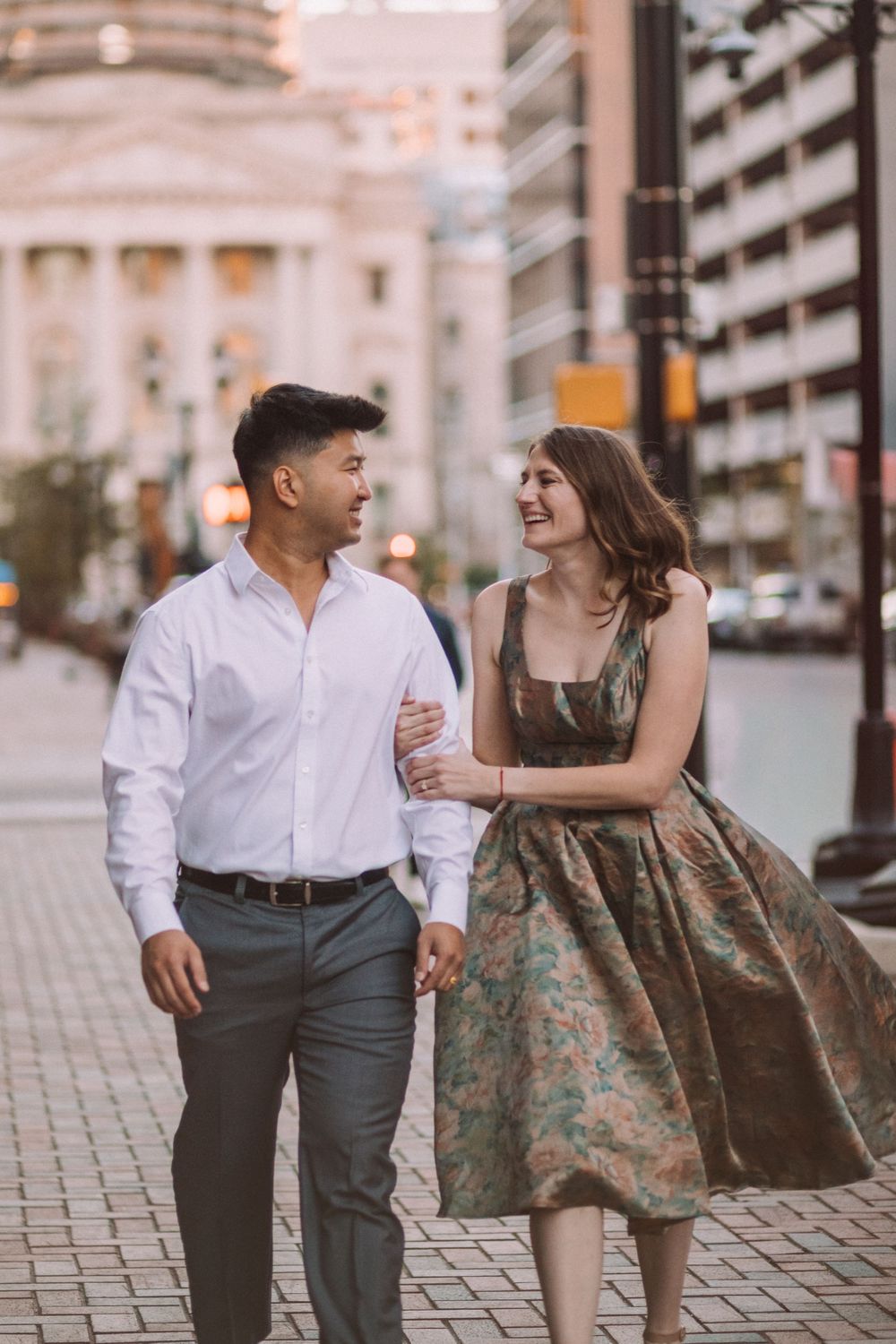 Couple walking and laughing together on cobblestone street during evening photoshoot.