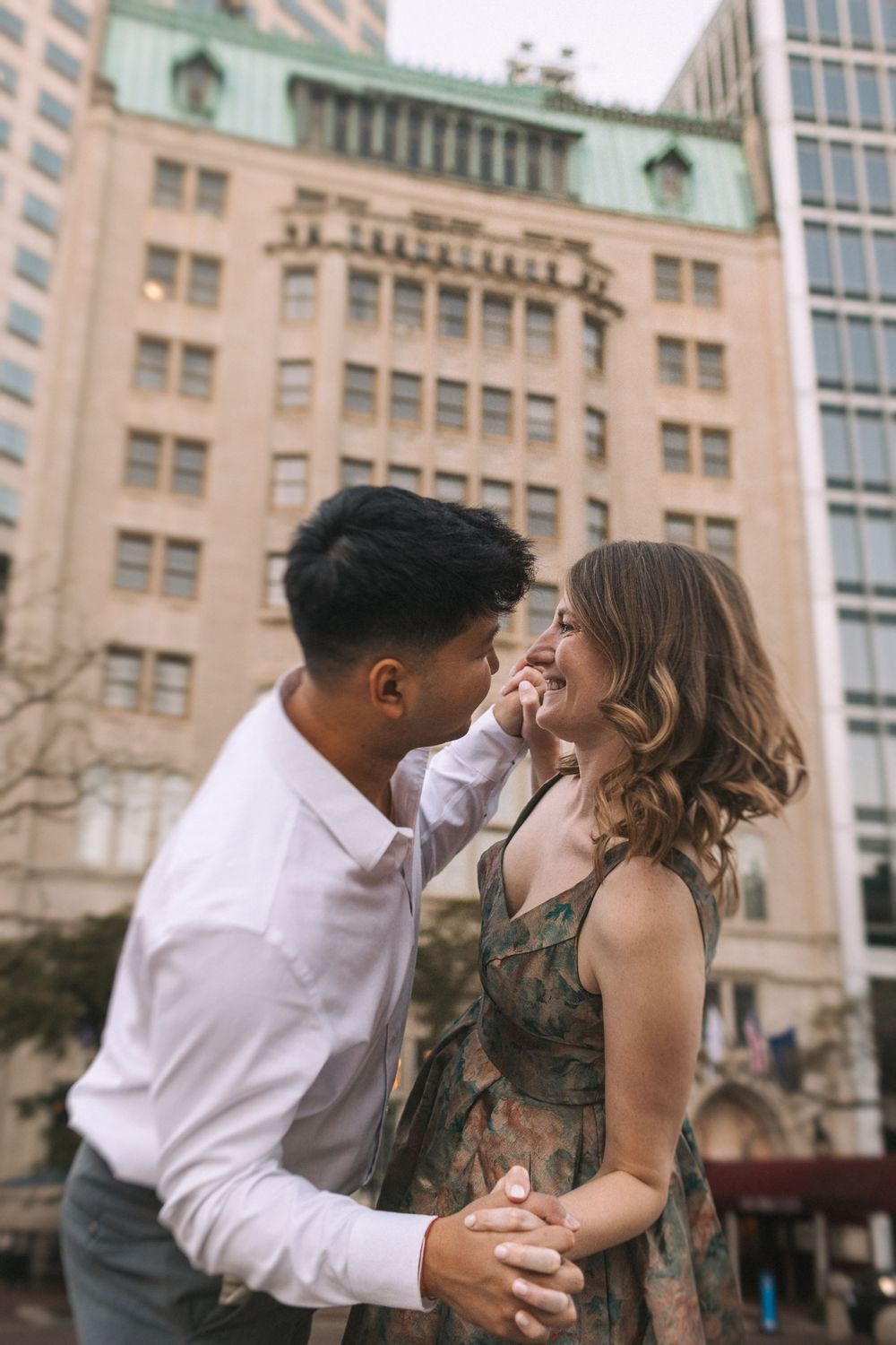 Playful couple sharing laughs and embraces against city backdrop during sunset.
