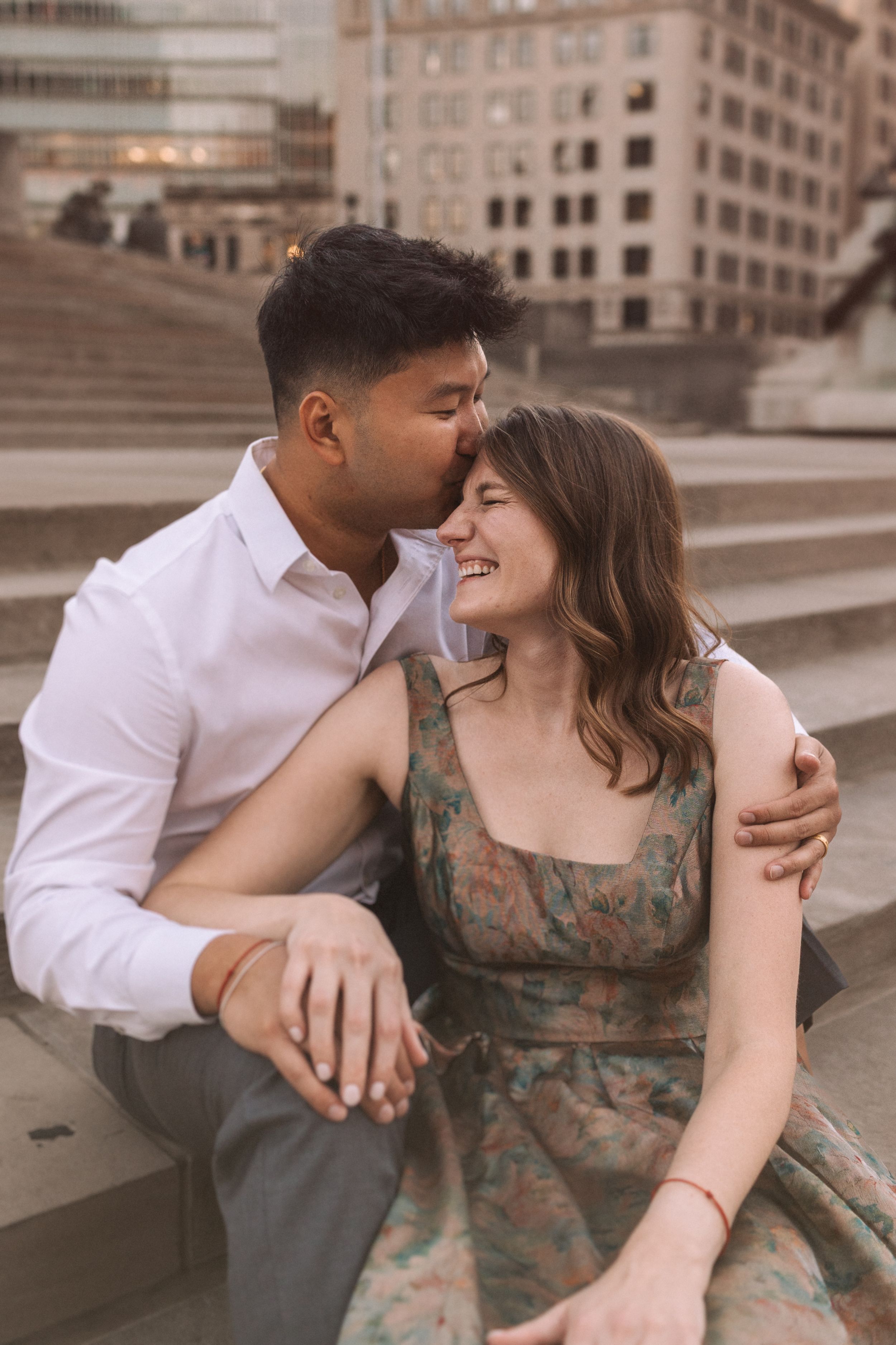 Sweet candid moments between couple sitting on stone steps in urban setting.