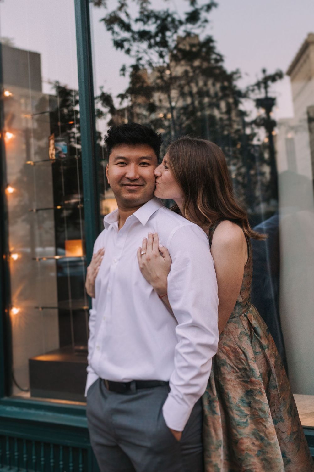 Romantic couple shares tender moments in front of a storefront window at sunset.