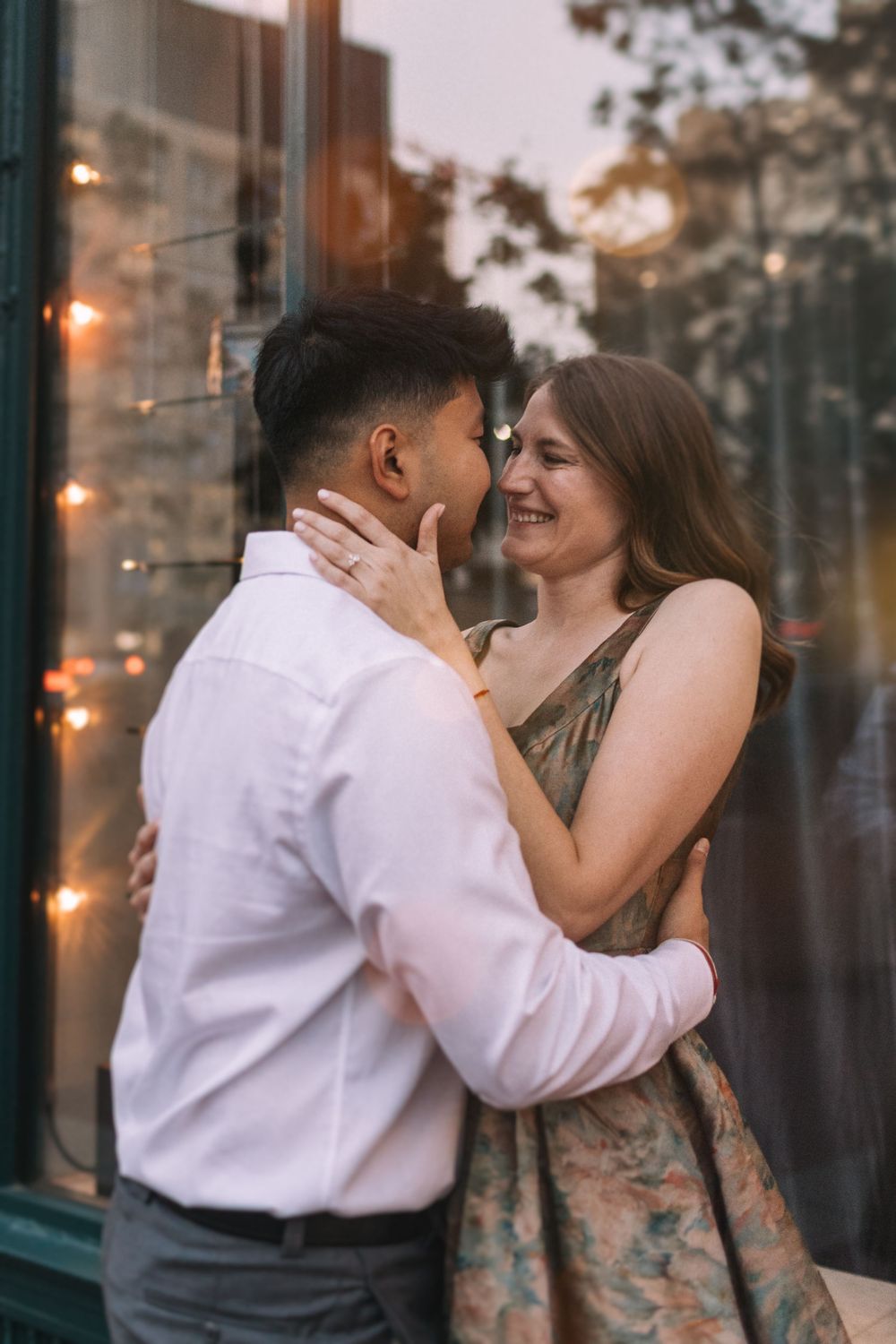 Couple shares affectionate moments against a window backdrop with twinkling lights.