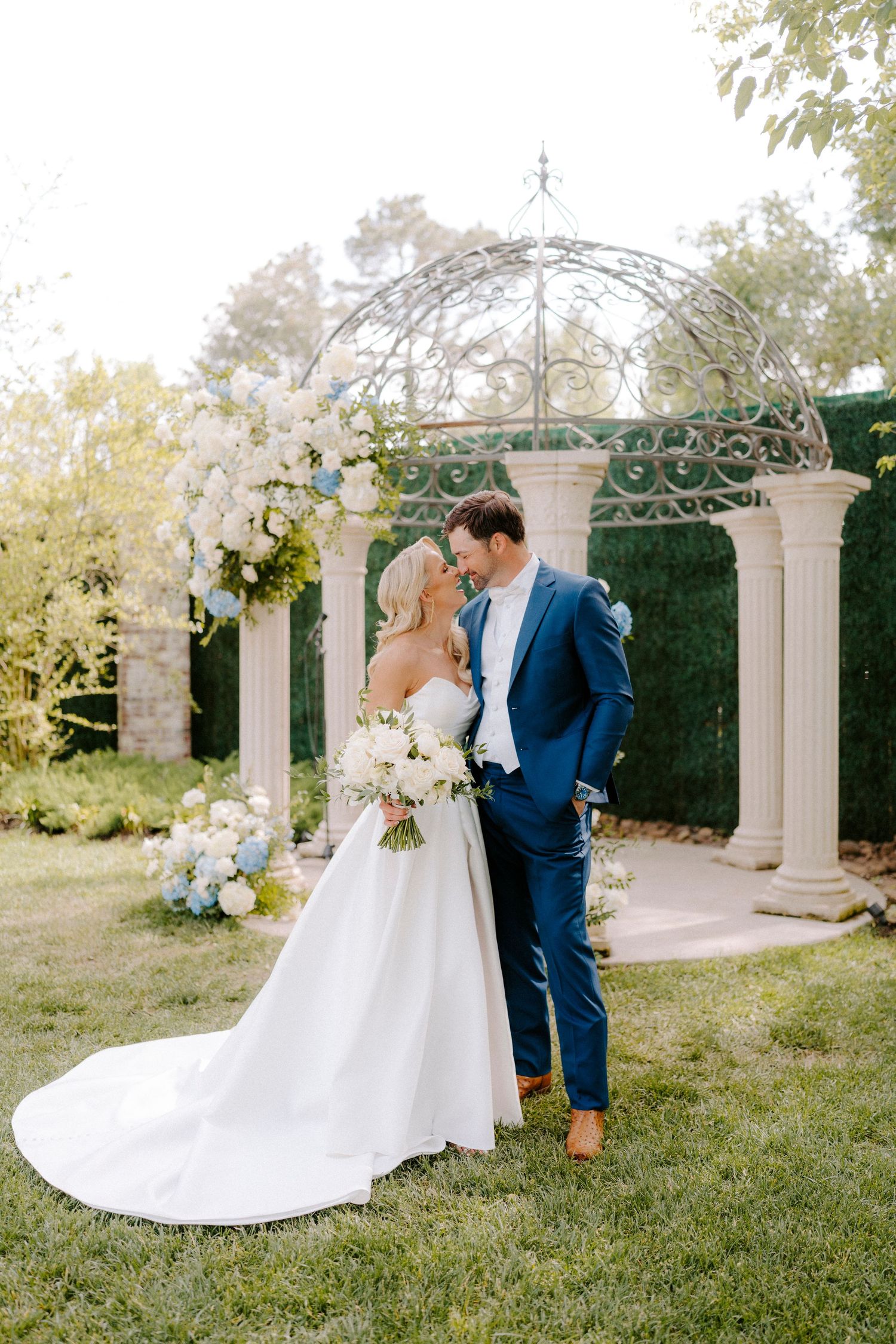 A romantic outdoor wedding moment captured in a garden setting with elegant white columns and lush greenery at The Ballroom at I-Street.