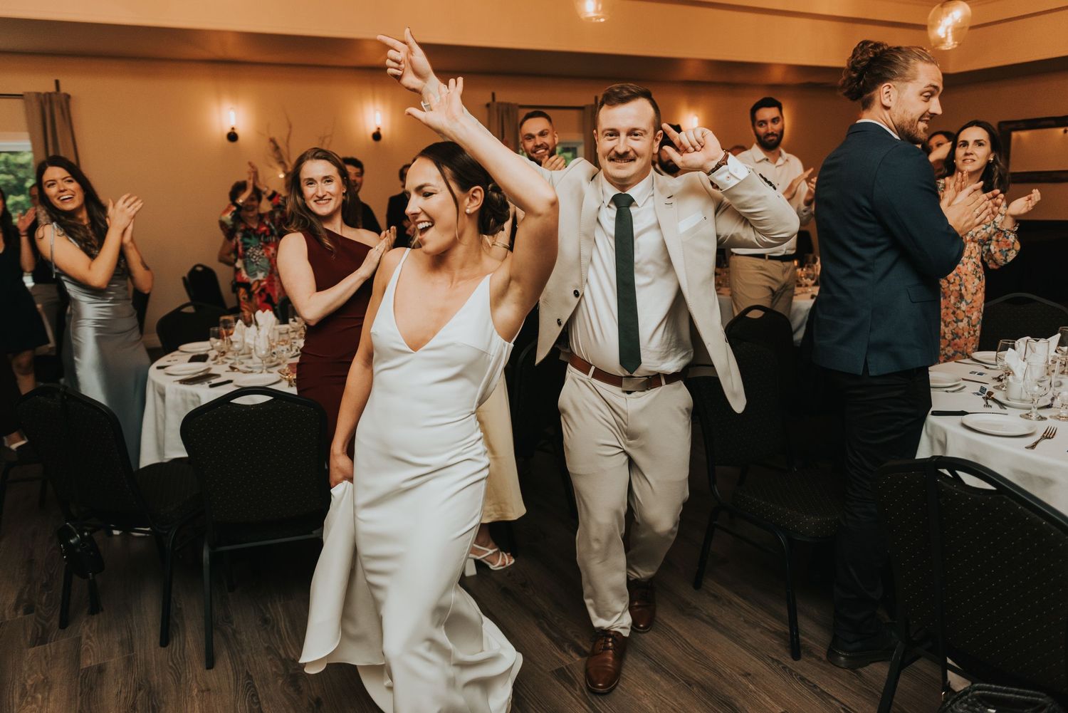Wedding guests dance and celebrate during a lively reception party in a warmly lit indoor venue.