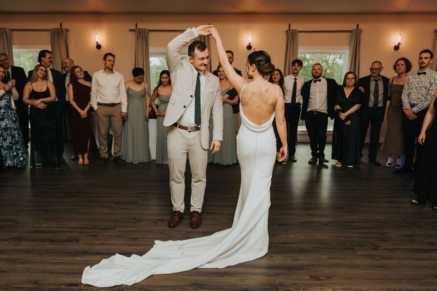A couple performs their first dance at a wedding reception surrounded by guests on a wooden dance floor.