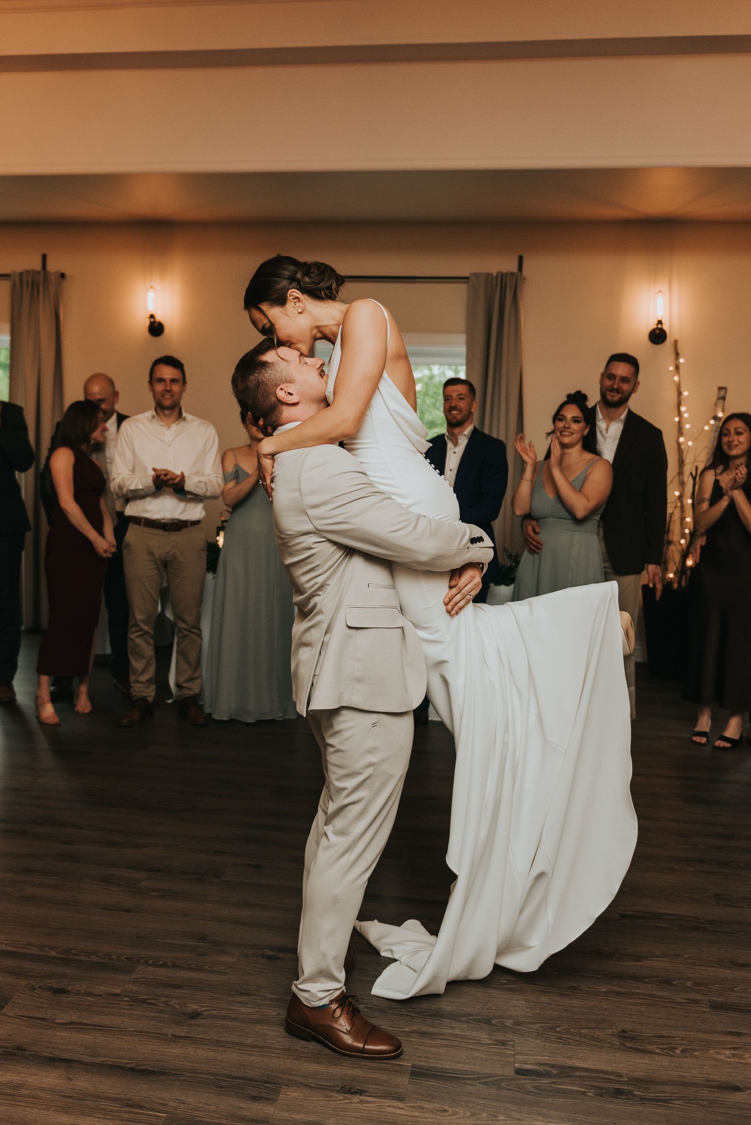 Couple performs an energetic dance move during their wedding reception on a wooden dance floor.