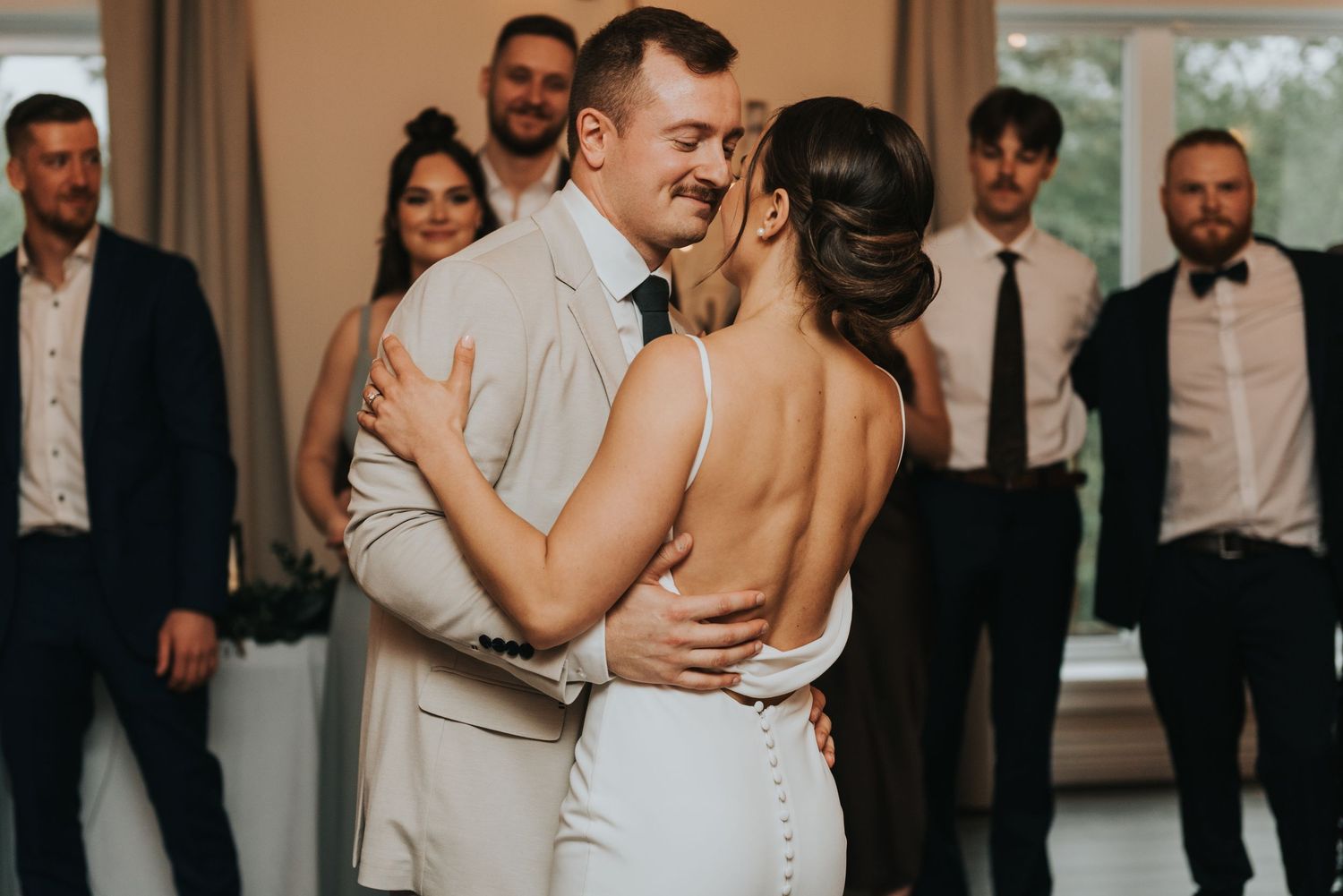 Wedding guests dance and embrace on a dimly lit dance floor during an elegant reception celebration.