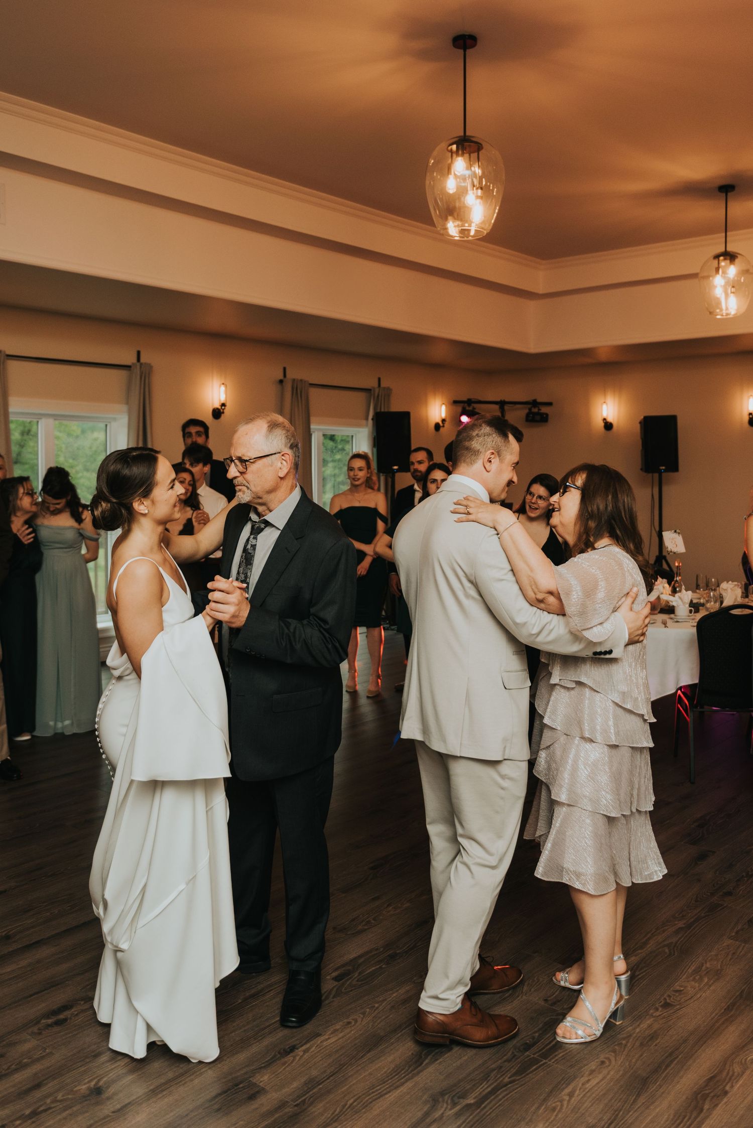 Wedding reception couples dancing in a warmly lit venue with hardwood floors and pendant lighting.