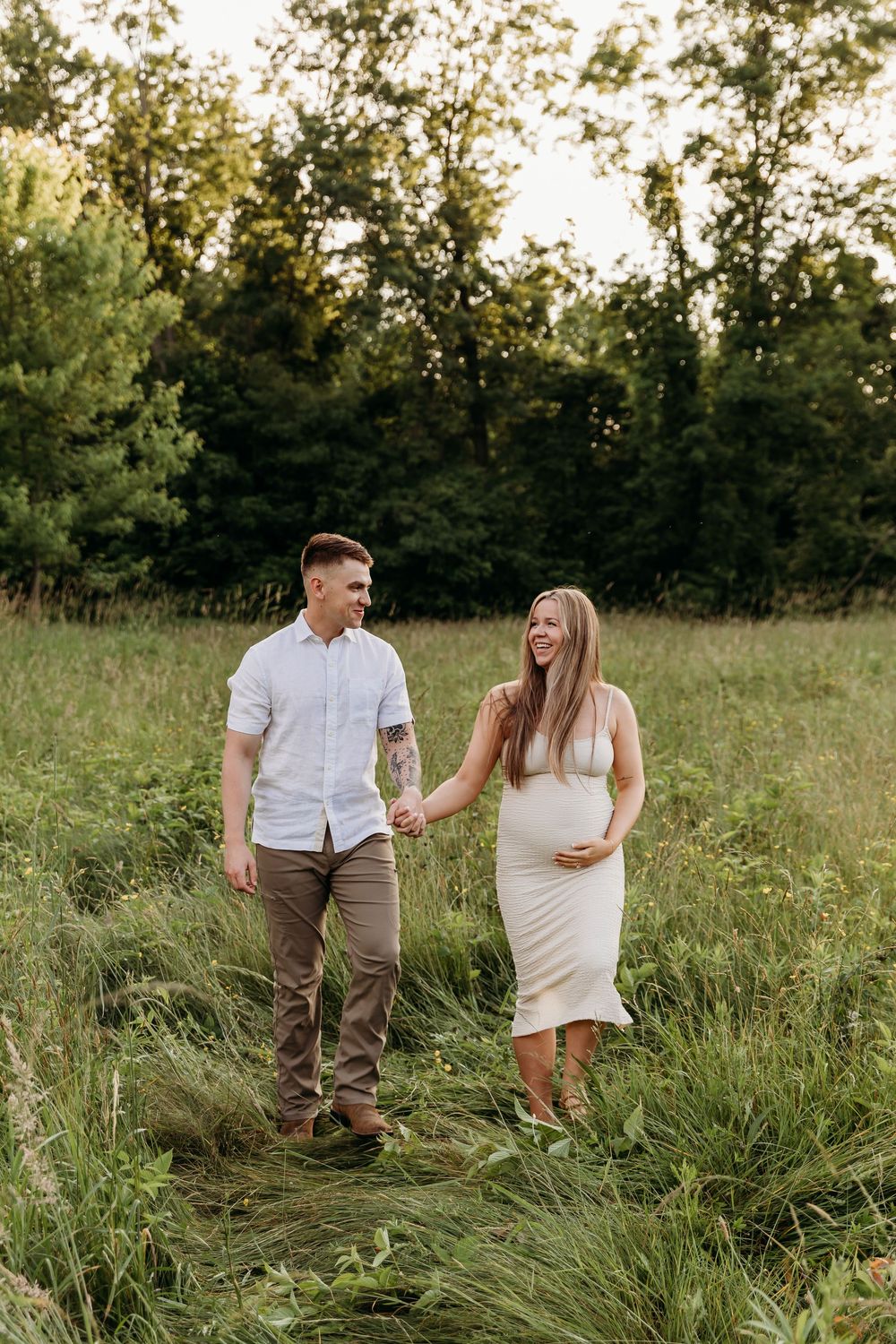 A couple shares joyful moments together in a sunlit meadow with tall grass during a summer photoshoot.