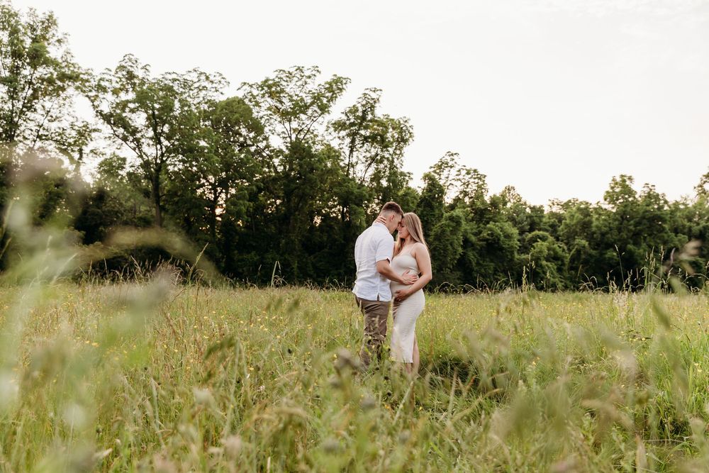 A couple in white outfits embraces in a sunlit meadow during a romantic outdoor photo session.