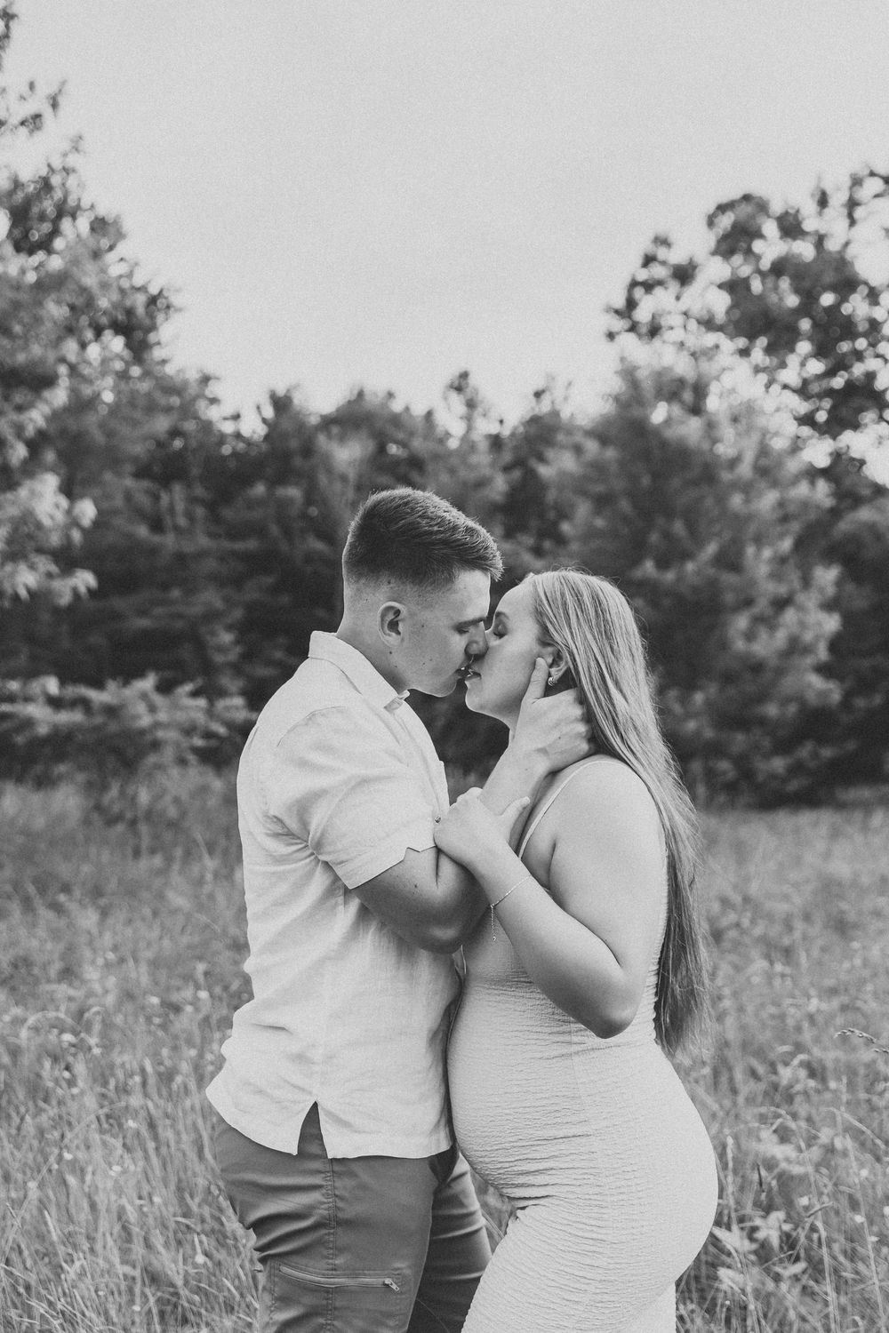 A romantic couple shares an intimate moment in a sunlit meadow wearing white and neutral tones.