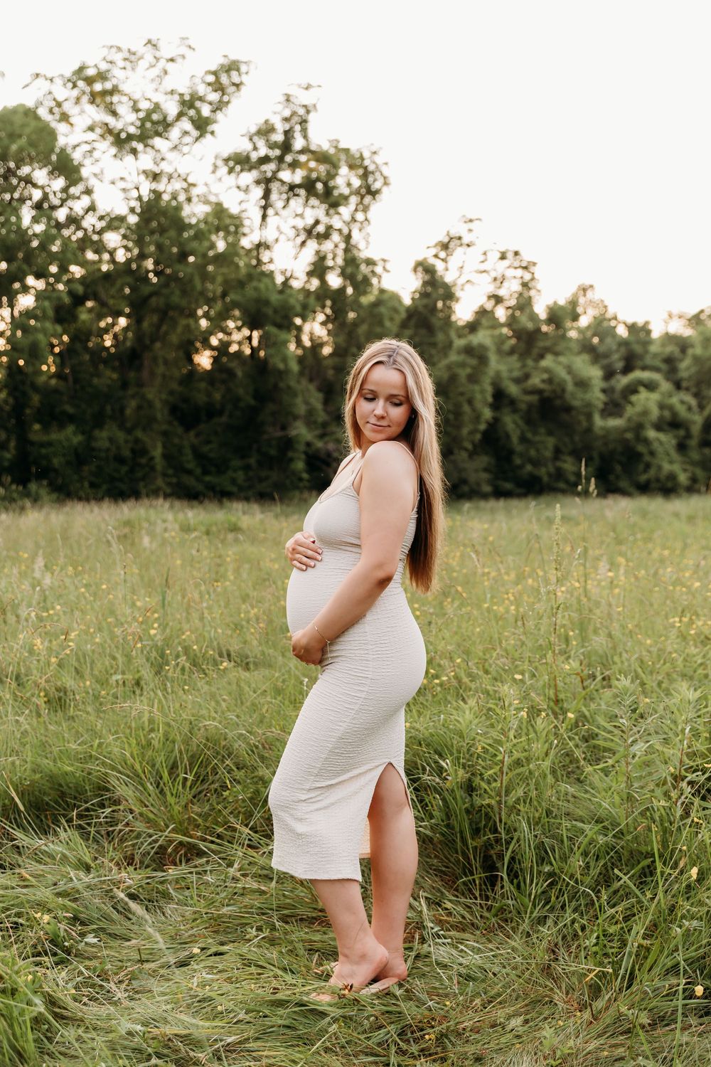 A woman in a white dress poses gracefully in a sunlit meadow during golden hour.