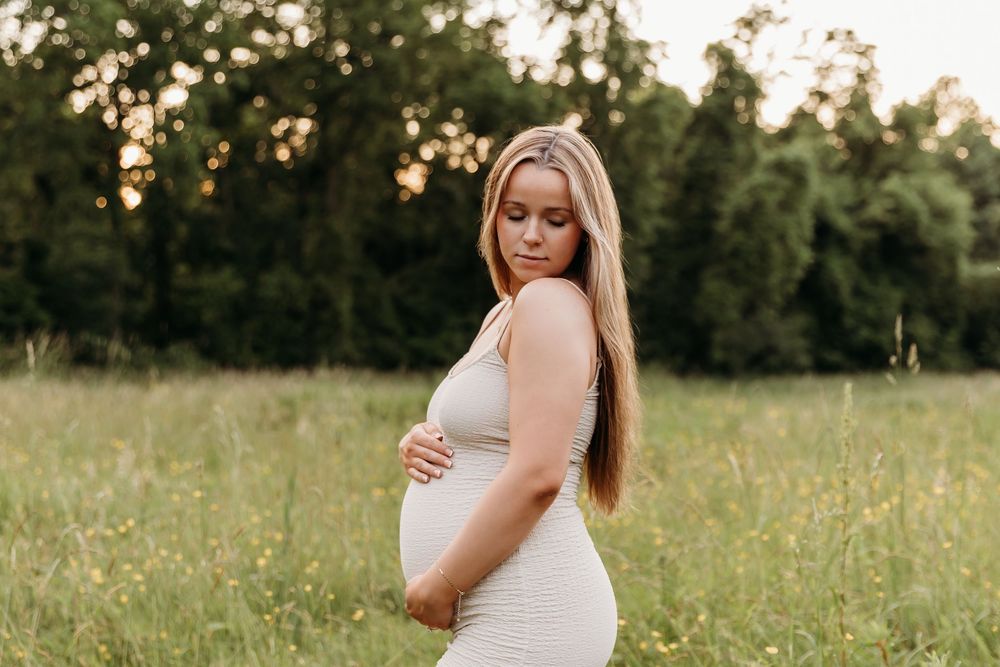 A person in a white dress poses in a sunlit meadow during golden hour.