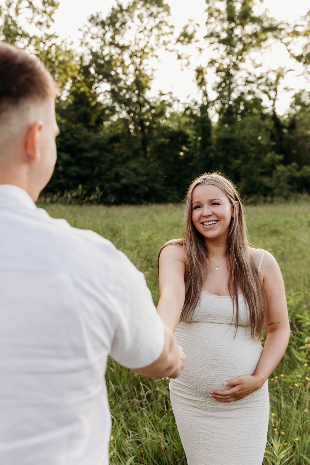 A couple shares joyful laughter together during a golden hour photoshoot in a sunlit meadow.