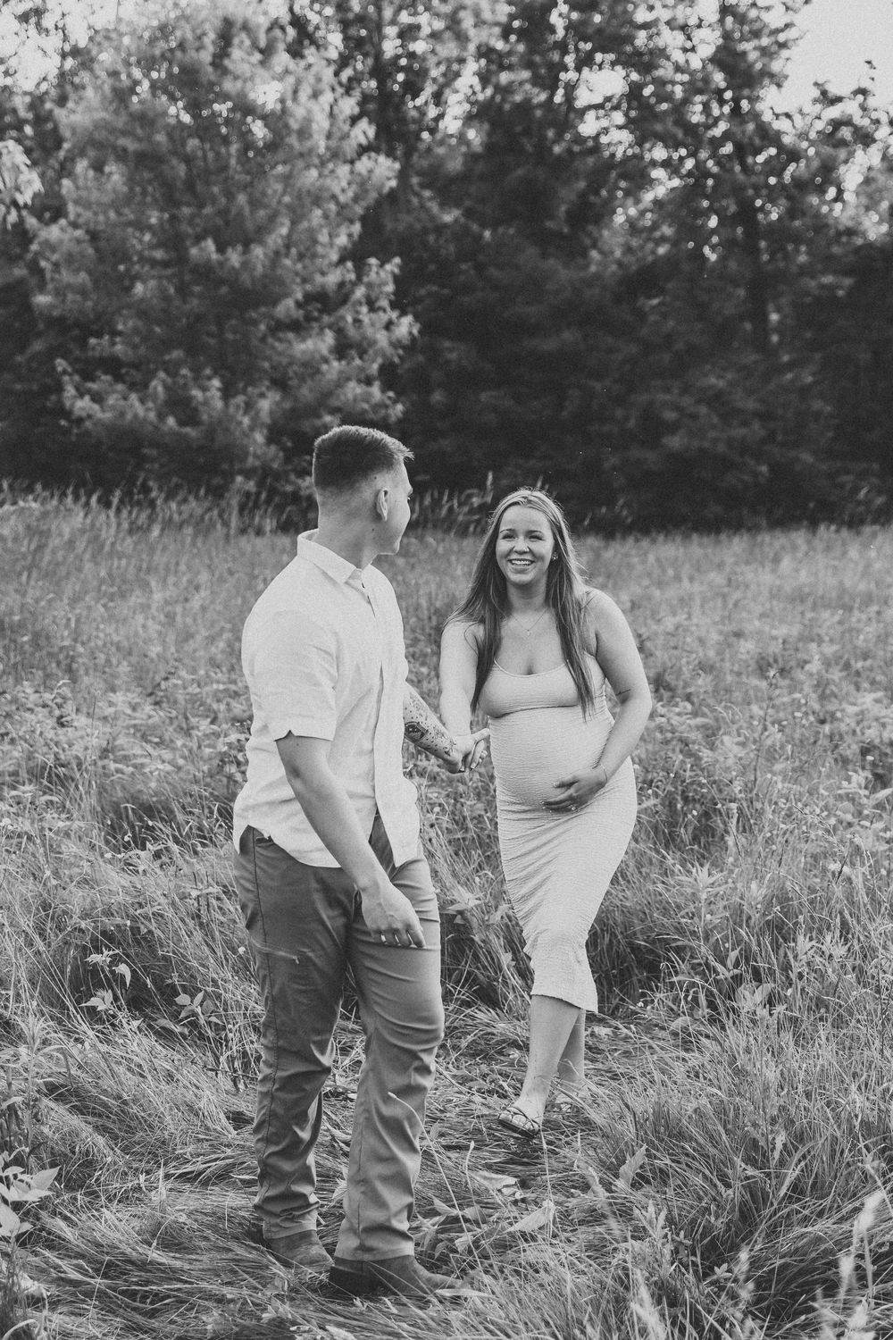 A couple shares intimate moments in a tall grass field in black and white photography.