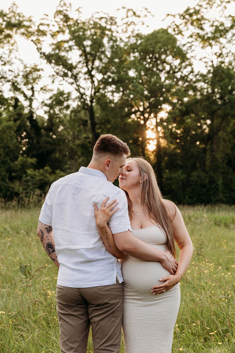 A romantic couple embraces tenderly in a sun-drenched field during a summer evening photoshoot.
