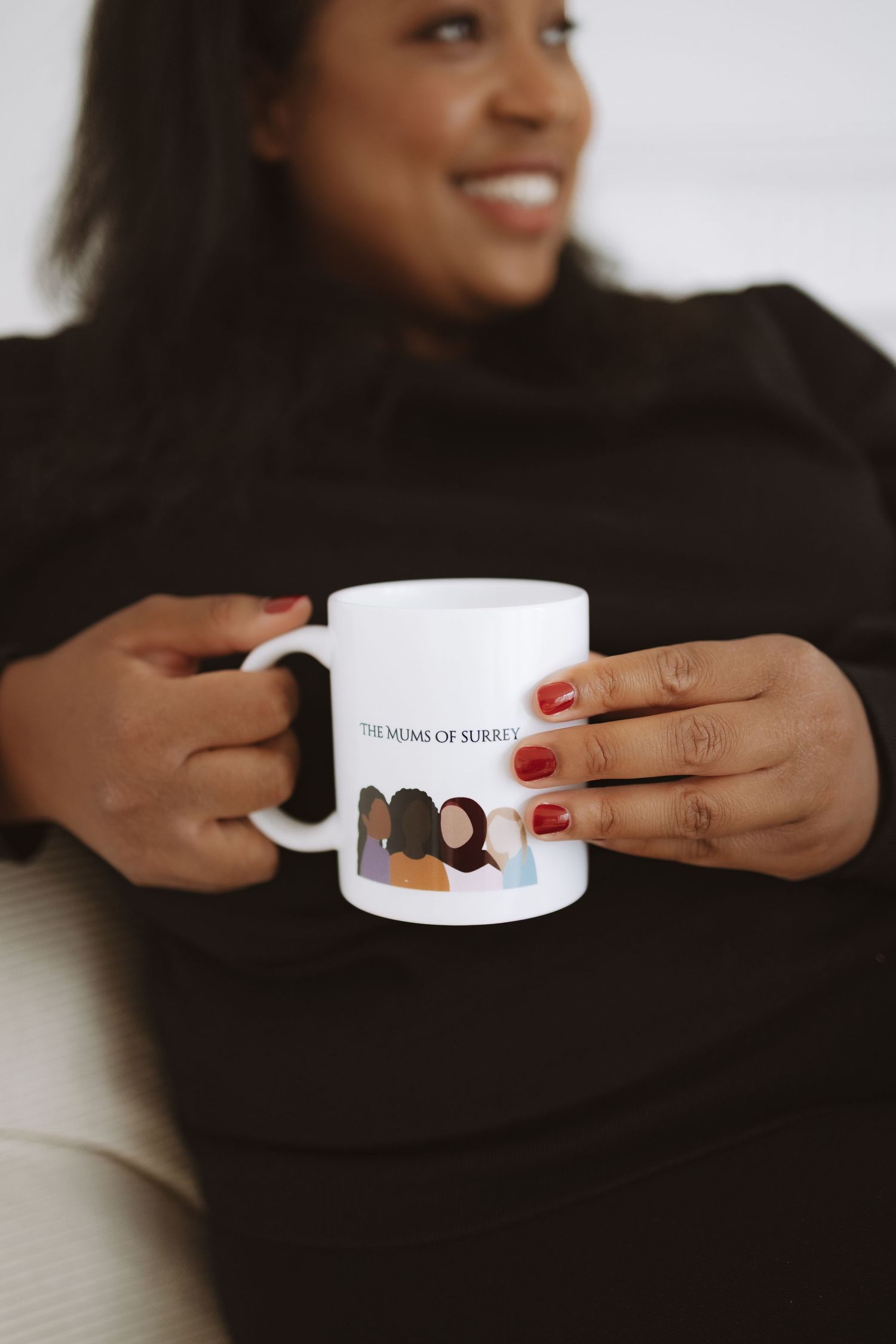 Hands with red nail polish hold and rotate a white ceramic mug displaying a black silhouette design.