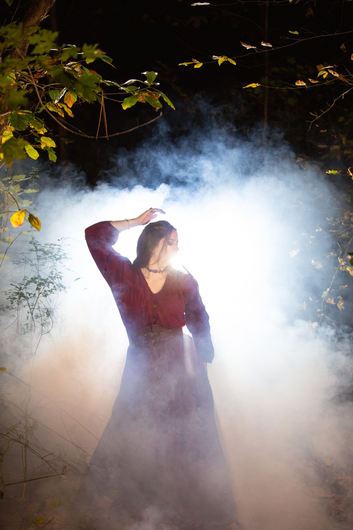A mysterious woman emerges through atmospheric fog and autumn leaves in a dramatic outdoor scene.