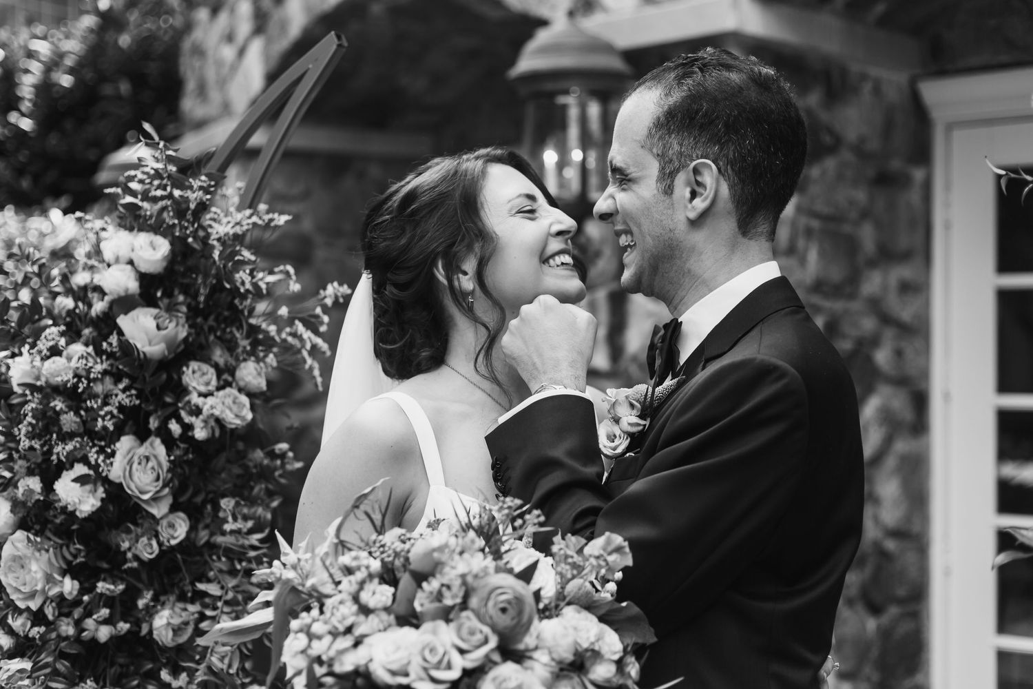 A romantic wedding couple shares an intimate moment outdoors surrounded by floral arrangements and natural light.
