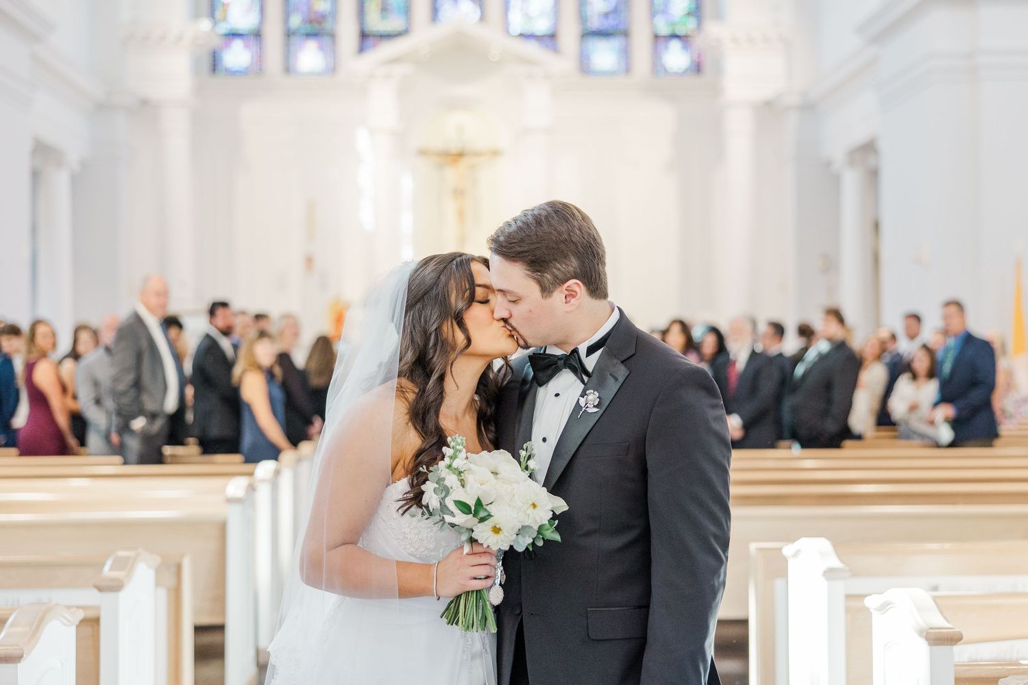 A couple shares a romantic moment in formal wedding attire at a bright, elegant church venue.