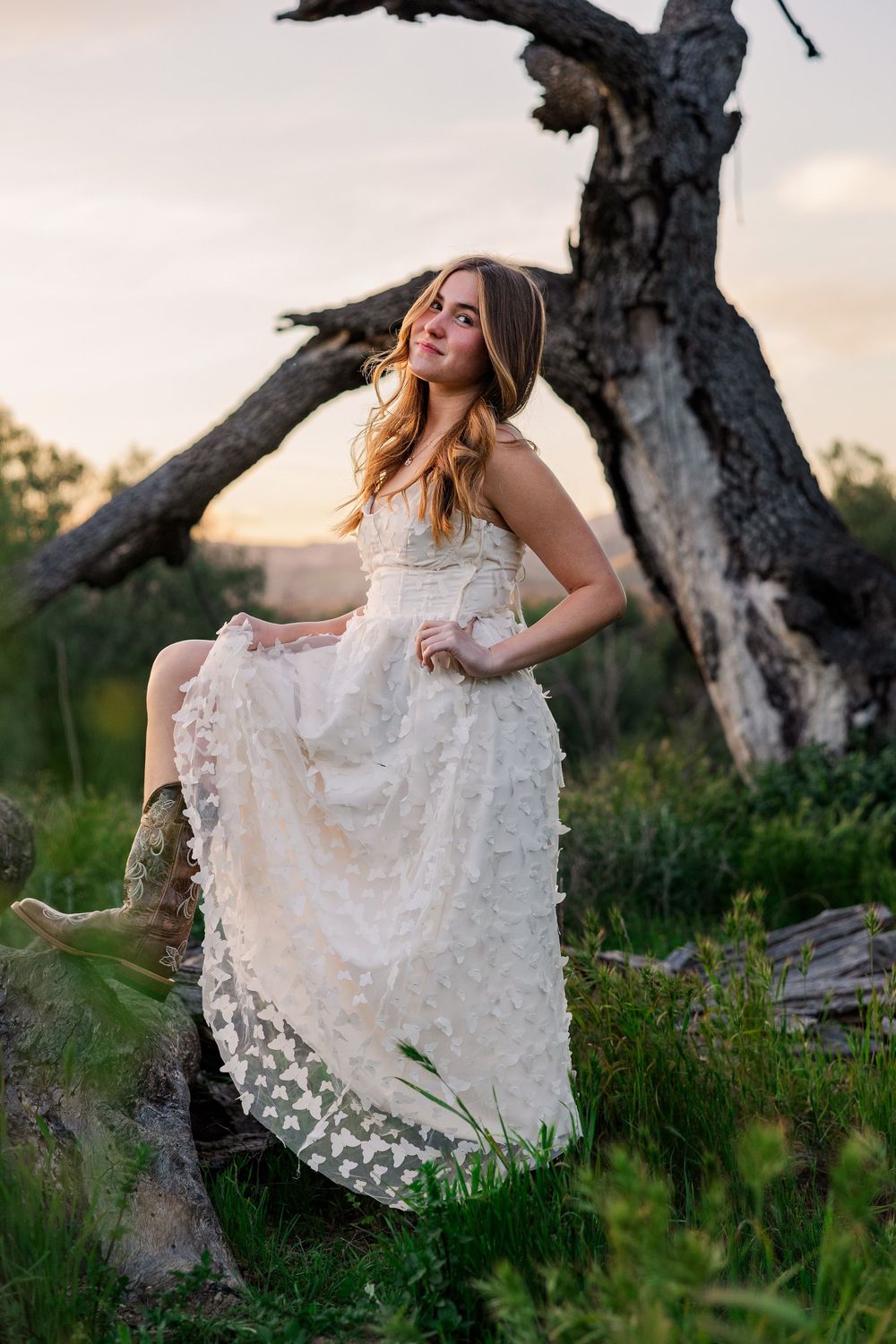 A dreamy outdoor portrait session in a white lace dress among tall grass and gnarled trees at sunset.