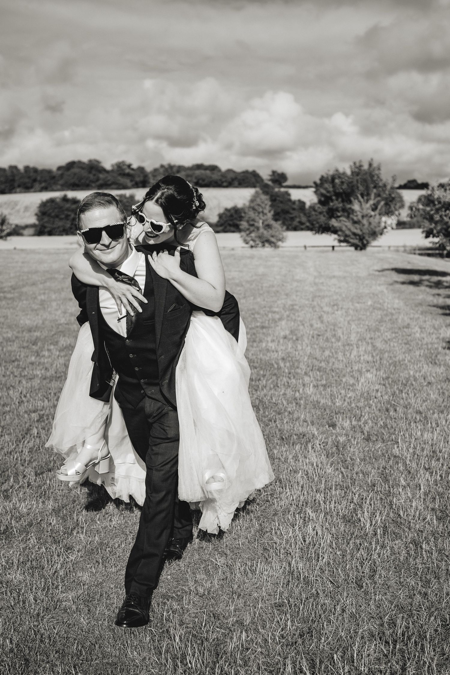 Black and white sequence of a couple in wedding attire playfully dancing and embracing in a grassy field.