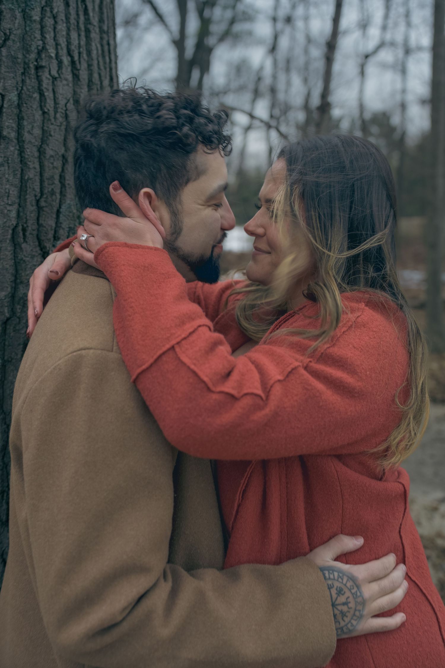 A romantic winter embrace between a couple wearing warm coats in a forest setting.