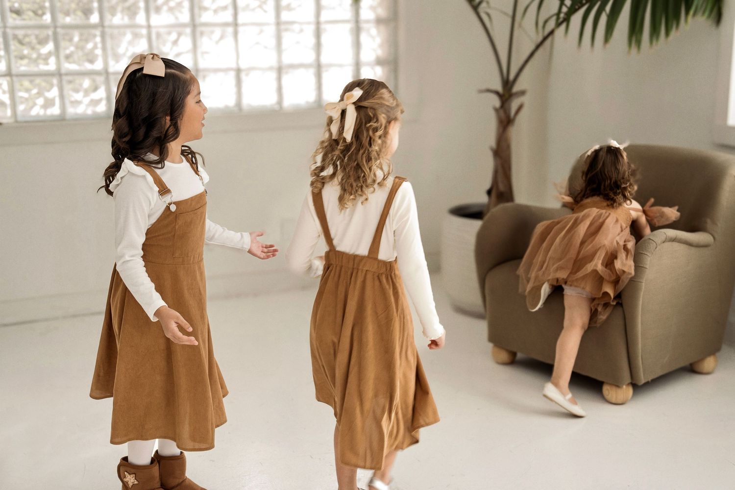 Two people in matching brown and white outfits pose playfully in a bright studio setting with natural lighting.
