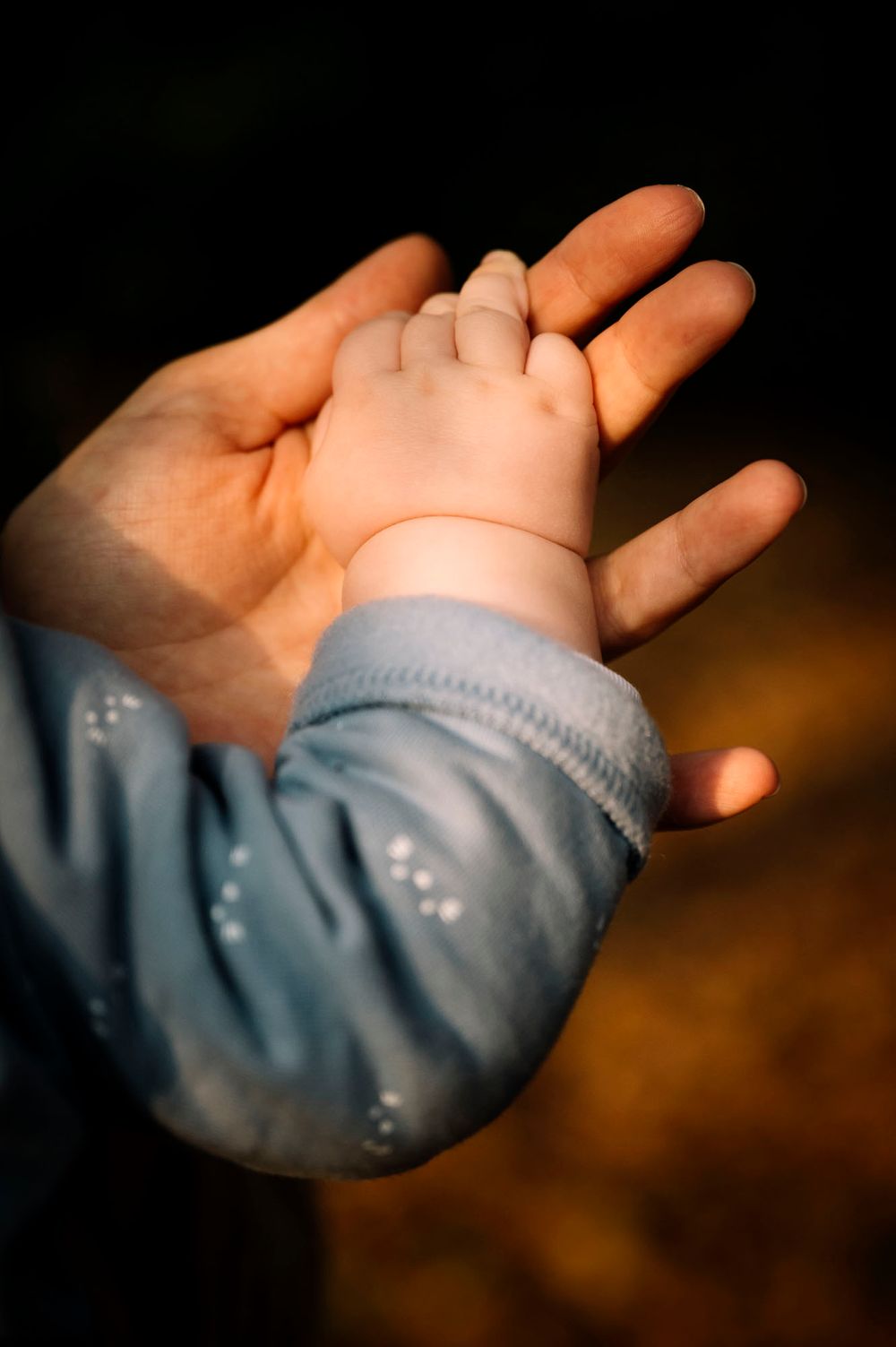 Primo piano di mani che cullano delicatamente un bambino vestito con morbidi indumenti blu.