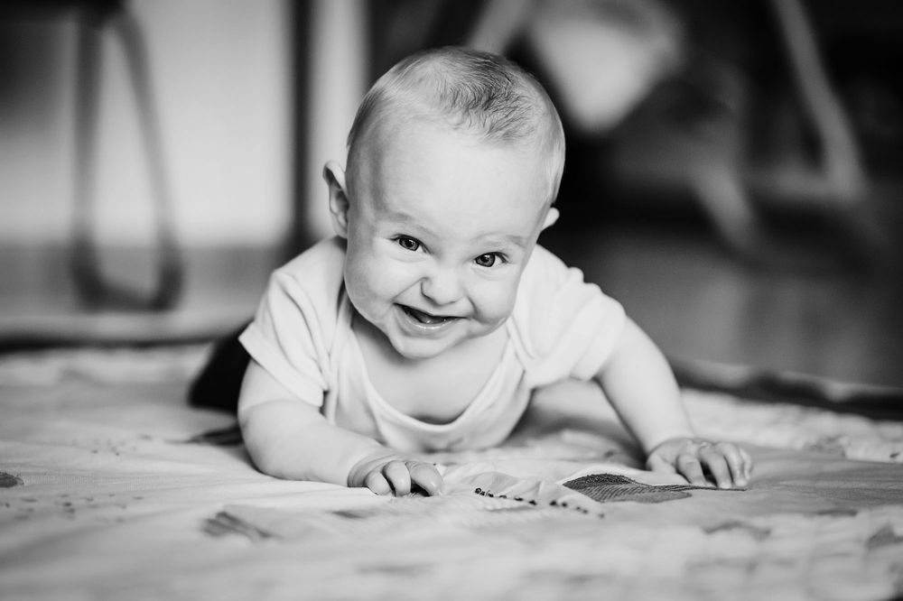 A black and white portrait of a crawling baby smiling at the camera.