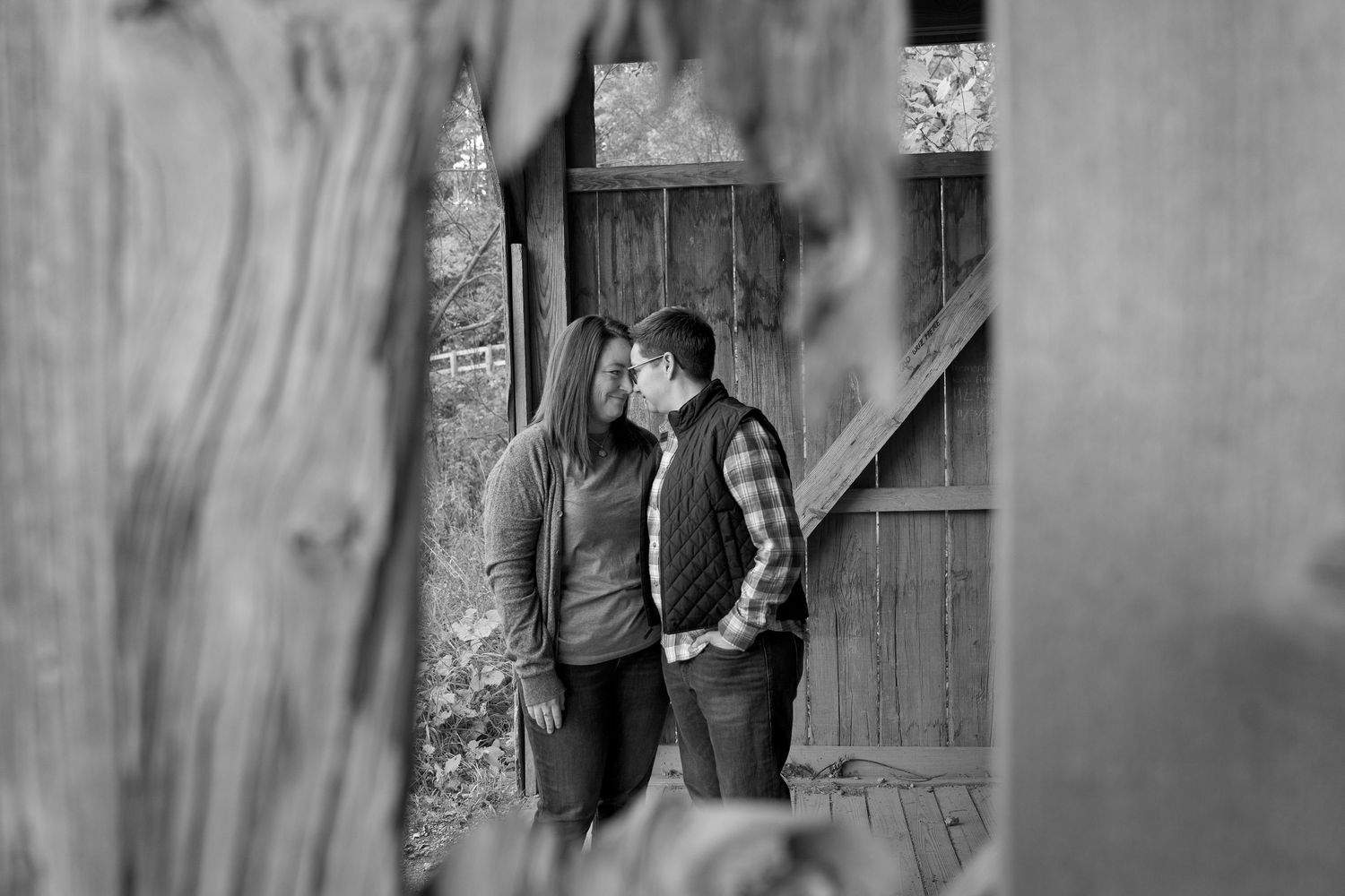 A romantic black and white photo of a couple sharing a tender moment against a rustic wooden door.
