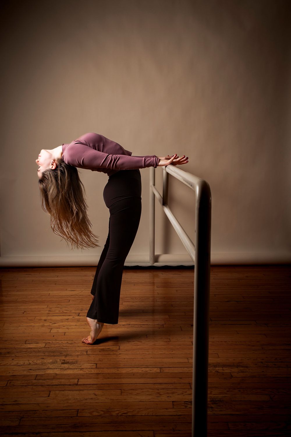 A sequence showing a dancer performing fluid movements while holding onto a ballet barre on a wooden floor.