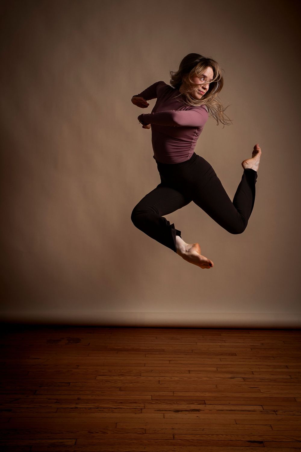 Athletic figure leaps and twirls through the air in a dramatic dance sequence on hardwood flooring.