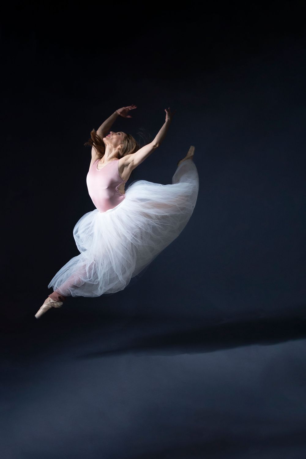 A ballet dancer in a white tutu performs a graceful leap sequence against a dark background, captured in multiple frames.